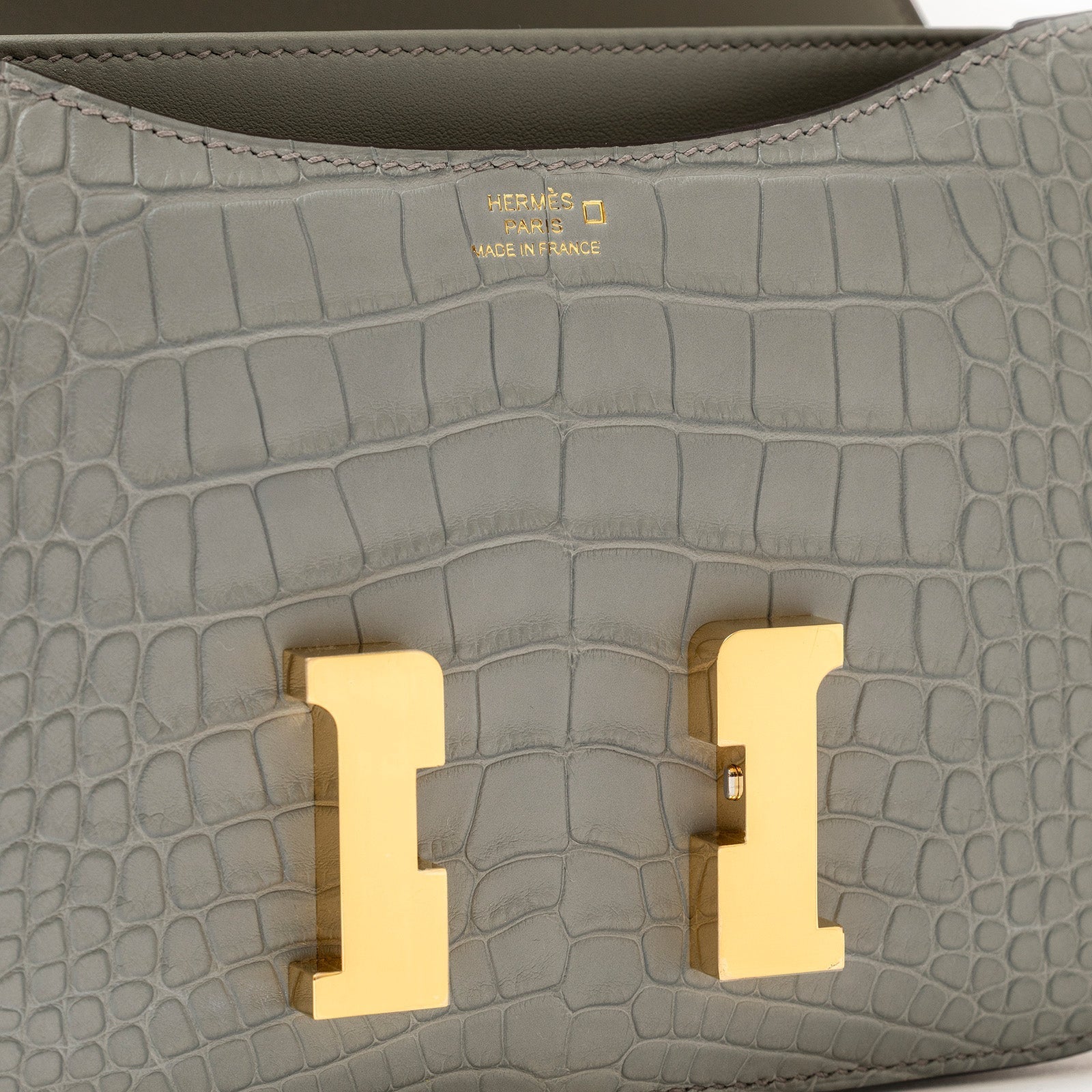 Close-up of Hermès Mini Constance 18 Gris Ciment Matte Alligator Gold Hardware showing gold clasp and texture