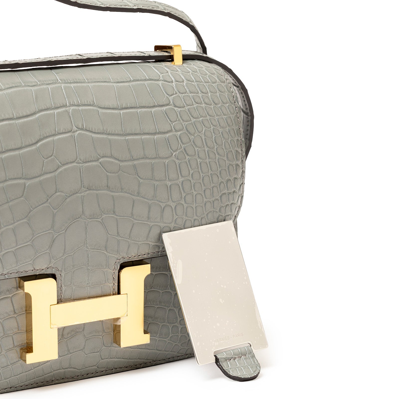 Close-up front view of Hermès Mini Constance 18 Gris Ciment Matte Alligator Gold Hardware with clasp detail and mirror