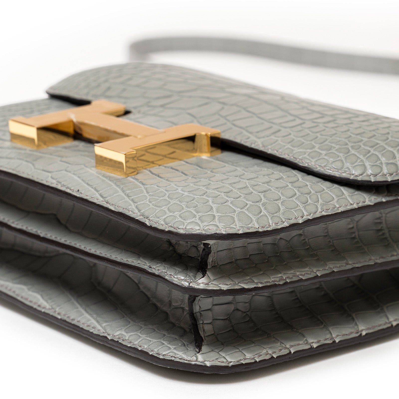 Close-up front angle of Hermès Mini Constance 18 Gris Ciment Matte Alligator Gold Hardware handbag showing texture and clasp detail