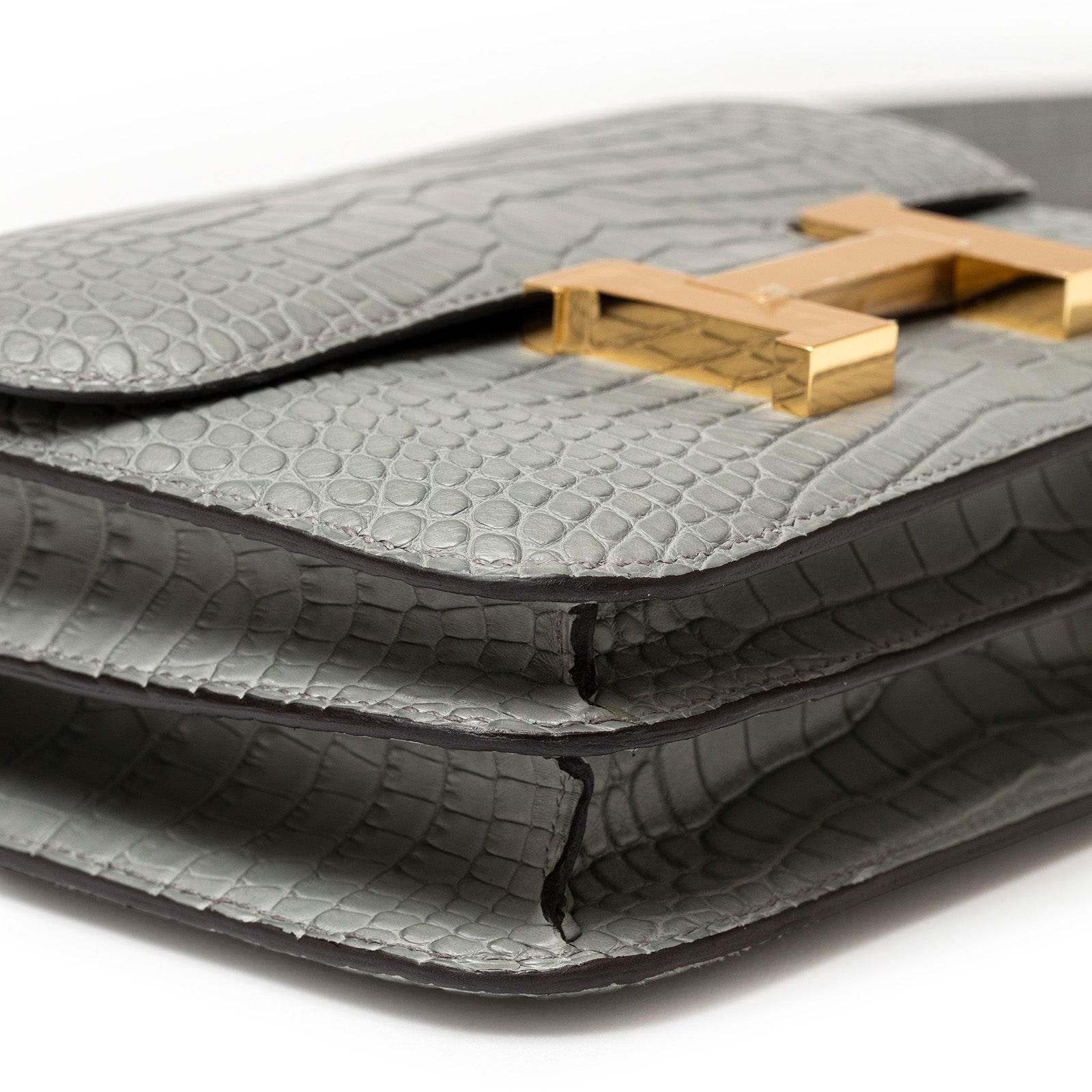 Close-up angled shot of Hermès Mini Constance 18 Gris Ciment Matte Alligator Gold Hardware showing texture and gold clasp detail