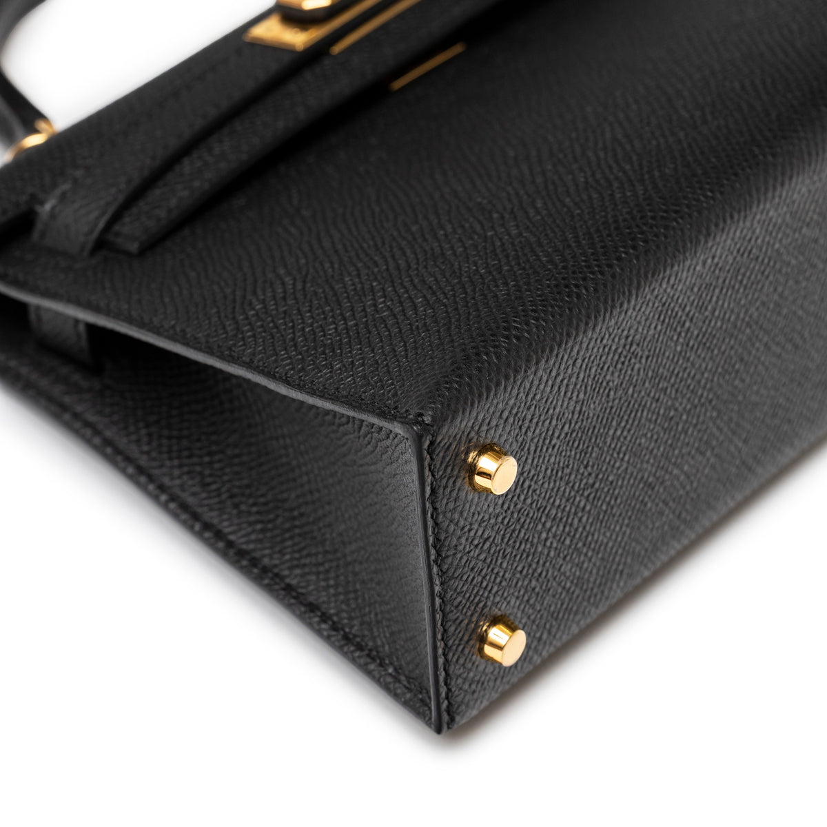Close-up of bottom corner on Hermès Mini Kelly II Sellier 20 Black Epsom Gold Hardware showing gold feet and textured leather