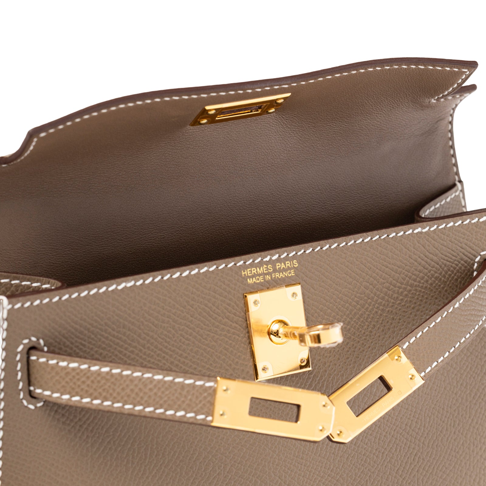 Interior view of Hermès Mini Kelly II Sellier Etoupe Epsom Gold Hardware highlighting gold lock and white stitching detail
