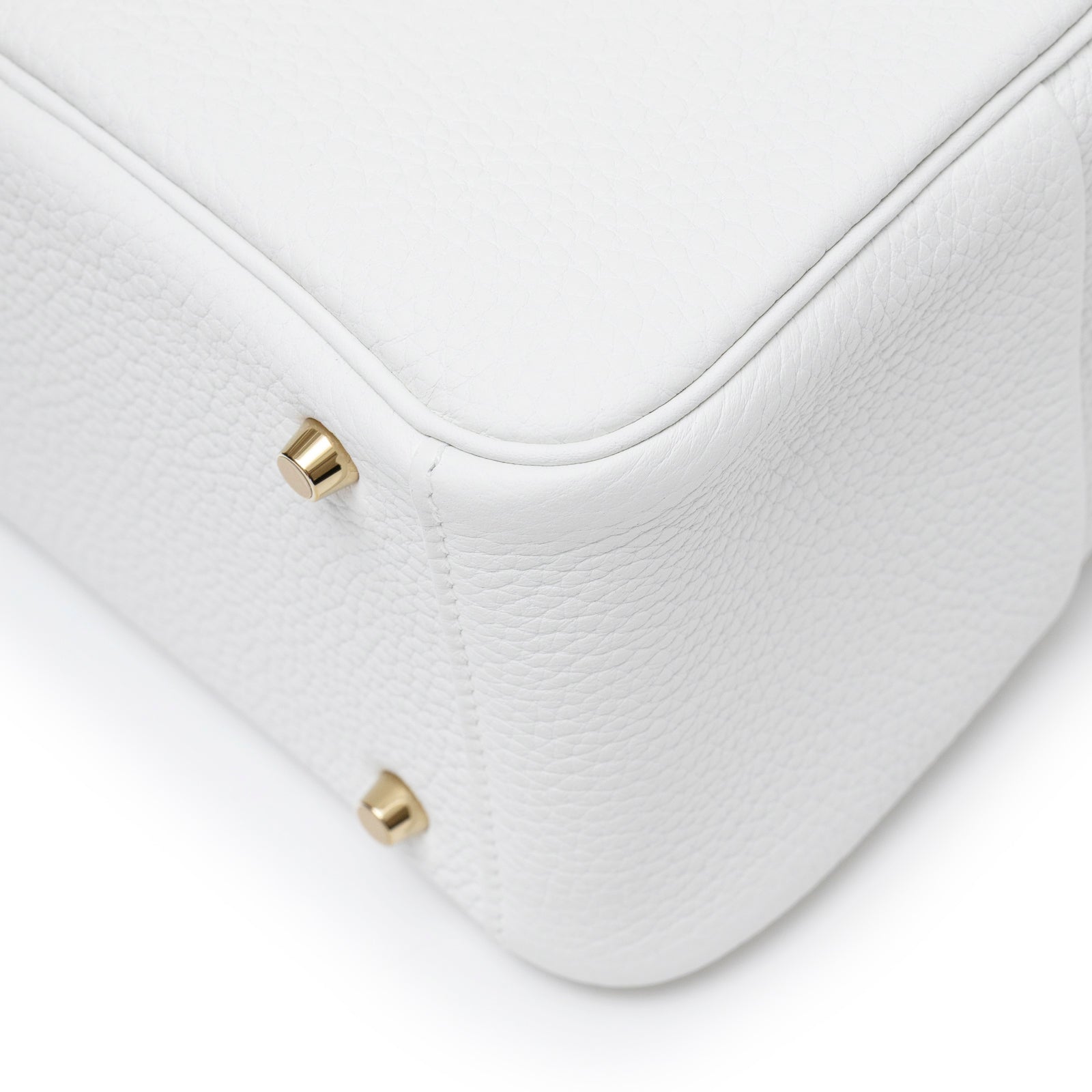 Close-up of the bottom corner of Hermès Mini Lindy II New White Clemence Gold Hardware showing texture and metal feet details