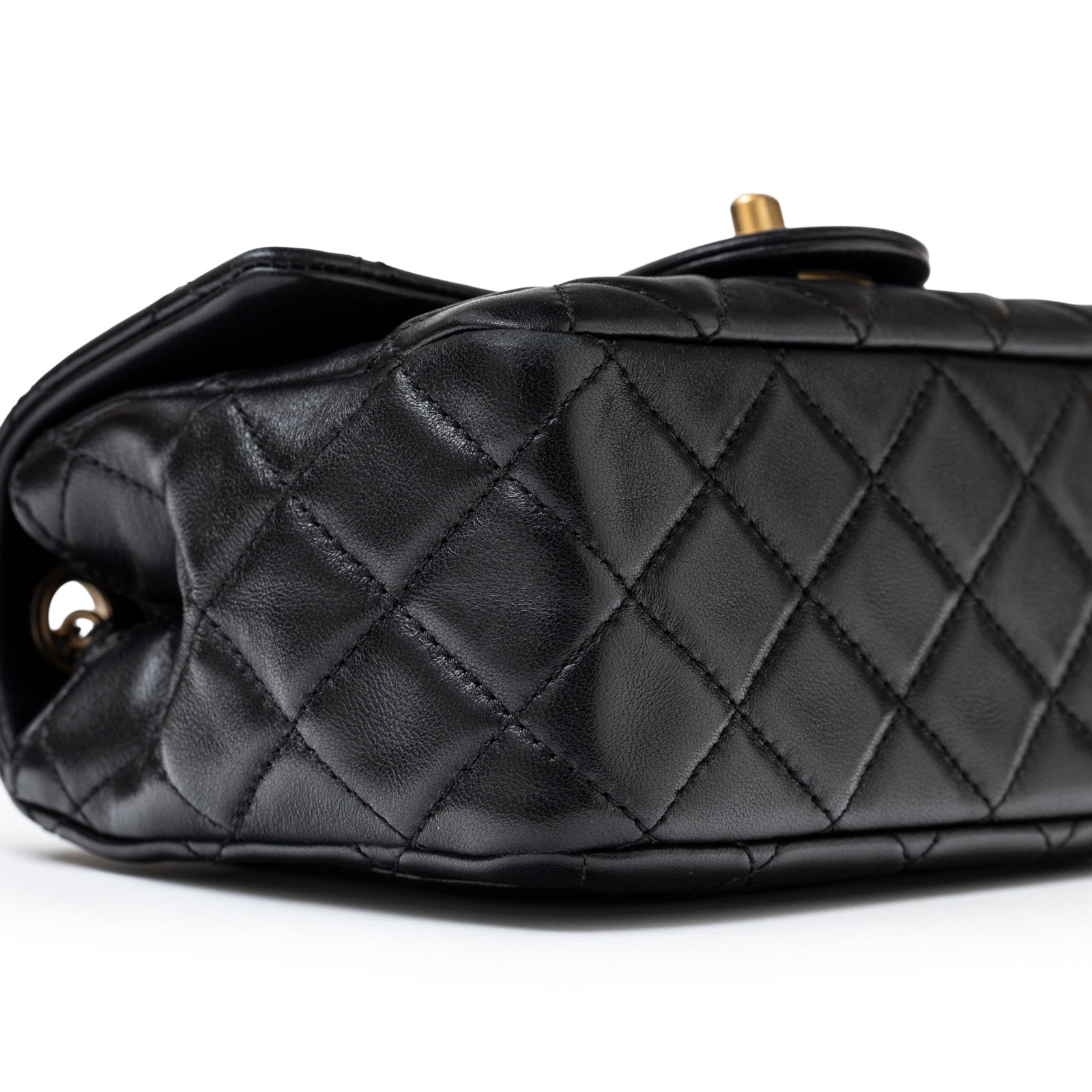Close-up side view of Chanel Mini Square Pearl Crush Flap Bag Black Lambskin Aged Brushed Gold Hardware showing quilted leather detail
