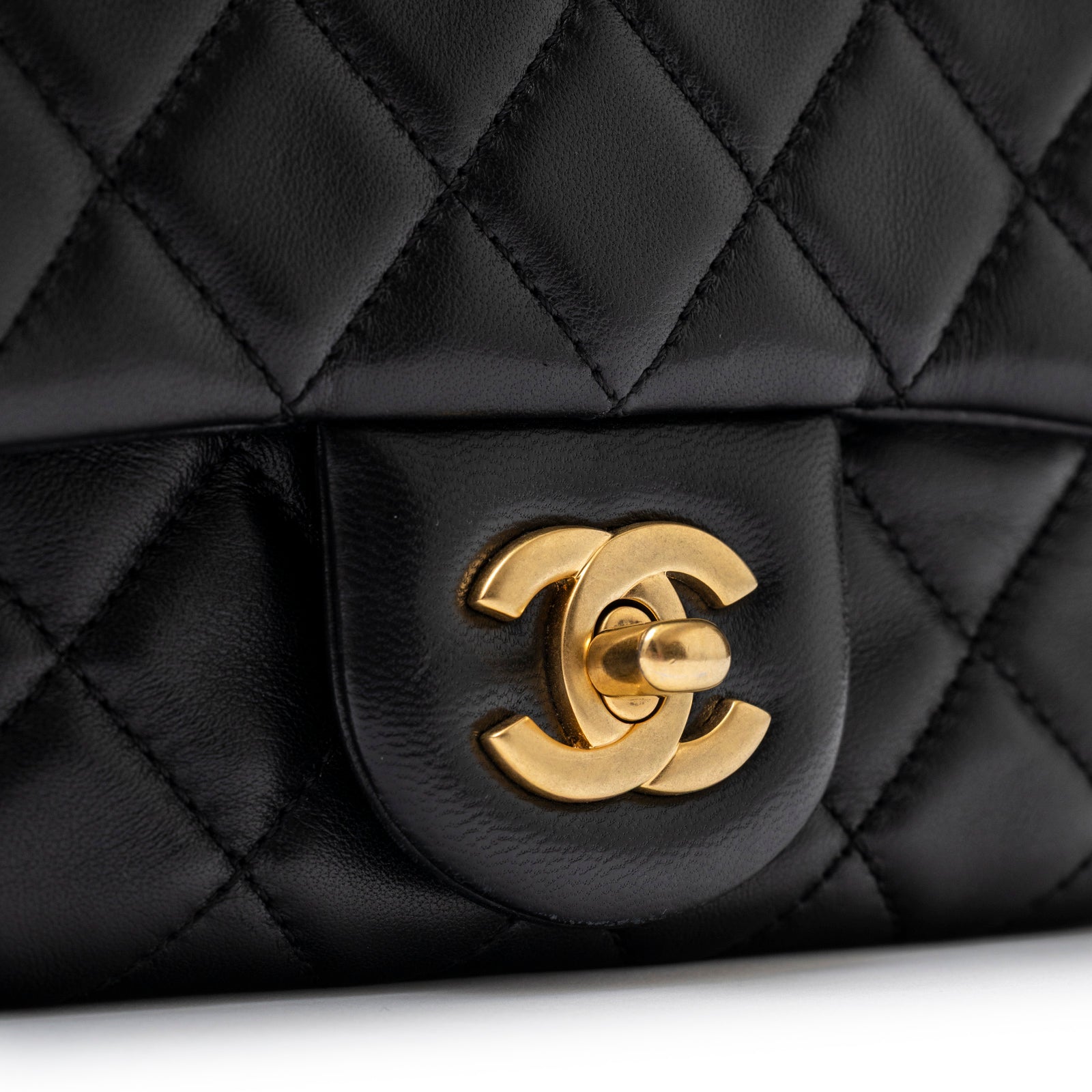 Close-up of gold hardware and black quilted lambskin leather on Chanel Mini Square Pearl Crush Flap Bag Black Lambskin Aged Brushed Gold Hardware