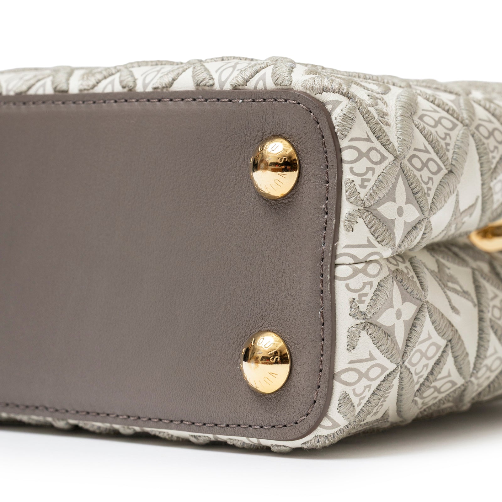 Close-up of base showing gold hardware and taupe calf leather on Louis Vuitton Since 1854 Embroidered Capucines BB Ecru/Taupe Calf Gold Hardware