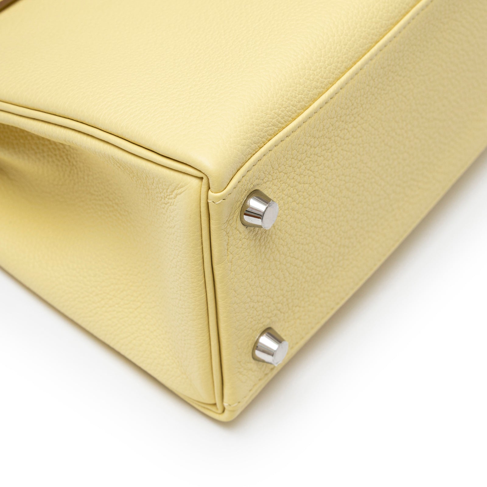 Close-up angled view of Hermès Kelly 25 Retourne Togo Jaune Poussin Palladium Hardware bottom corner showing textured leather and hardware studs