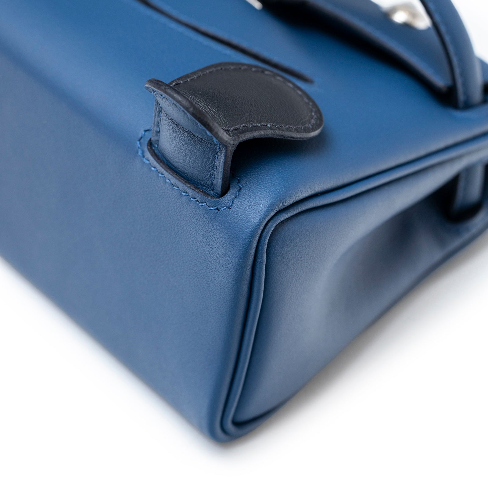 Close-up of bottom corner and black leather detail on Hermès Quelle Idolle Kelly Doll Bleu Tie and Caban Swift Palladium Hardware bag