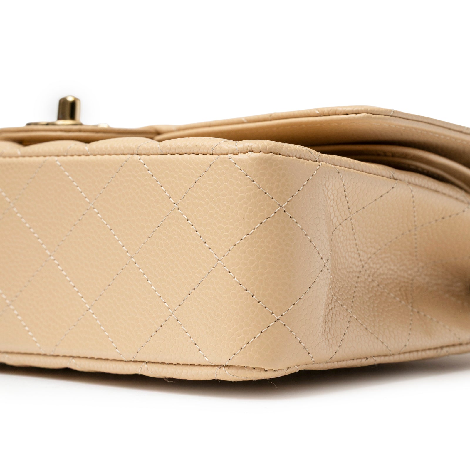 Close-up angled view of beige leather stitching on Chanel Classic Flap Medium Caviar Beige Gold Hardware bottom corner.