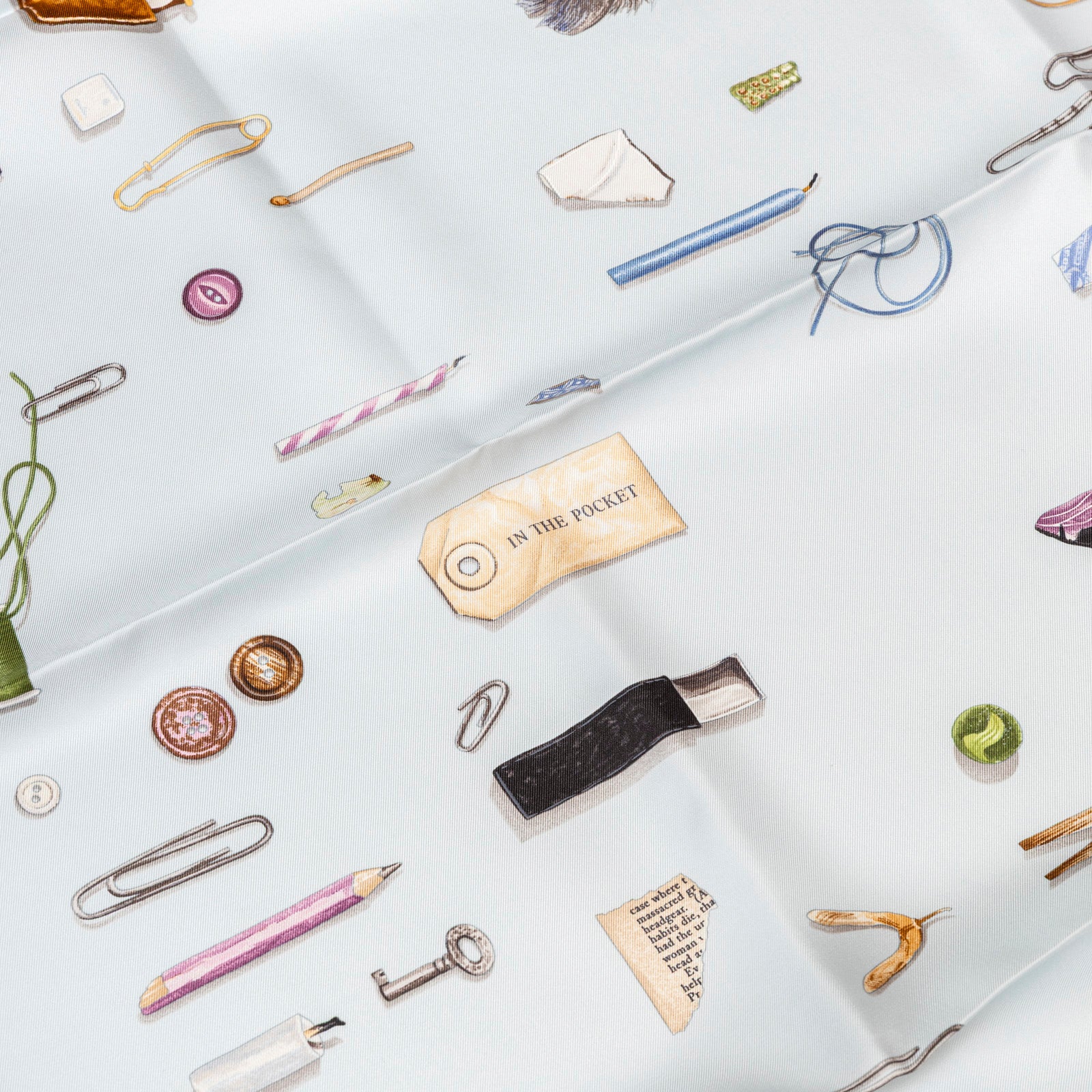 Close-up angled view of Hermès Carre Scarf 90 In The Pocket Blue Glacier/Blue Pale showing illustrated pocket items pattern