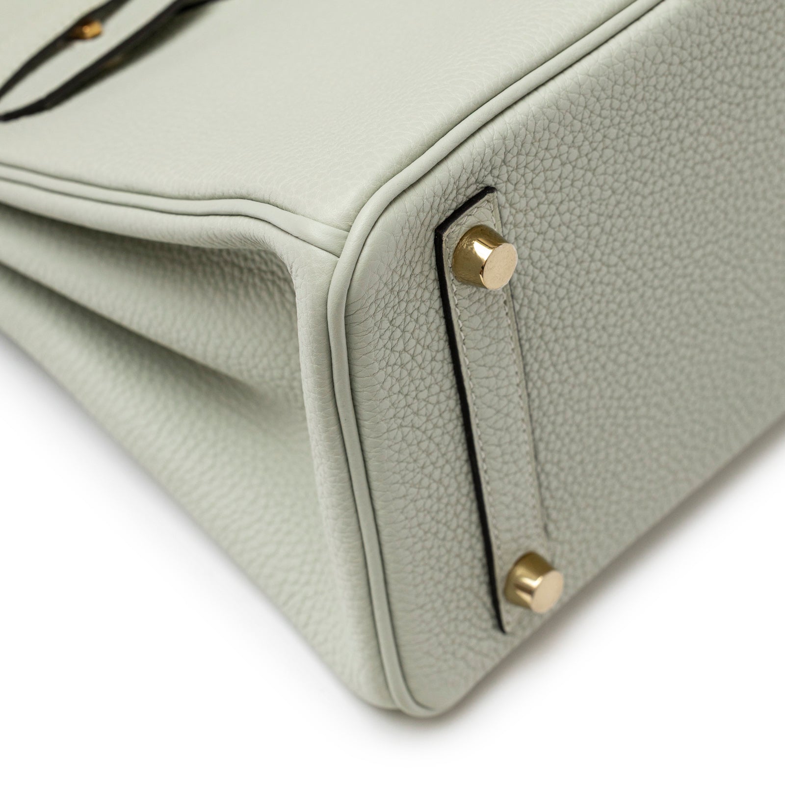 Close-up angled view of bottom corner and gold hardware studs on Hermès Birkin 25 Gris Neve Togo Gold Hardware