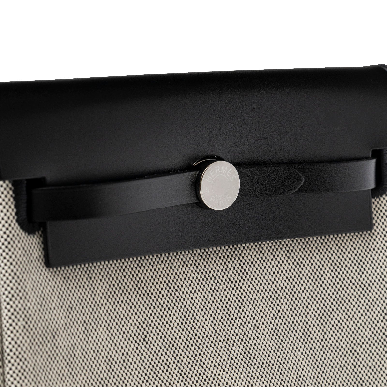 Close-up angled view of Hermès Mini Herbag Zip 20 Ecru/Black Toile and Vache Hunter Palladium clasp detail