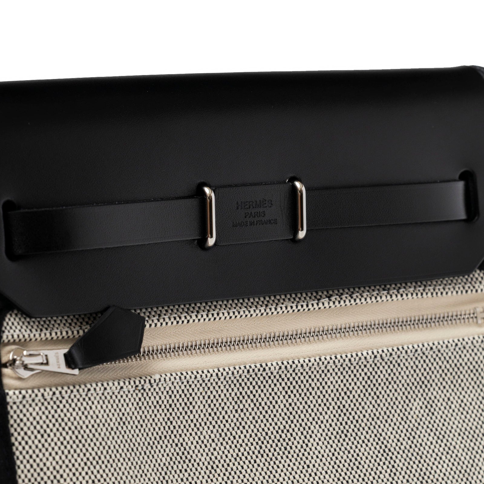 Close-up angled view of Hermès Mini Herbag Zip 20 Ecru/Black Toile and Vache Hunter Palladium Hardware zipper and leather trim detail