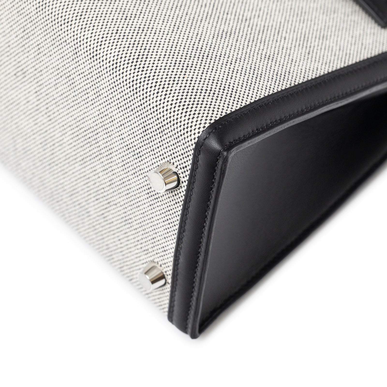 Close-up of bottom corner with palladium feet on Hermès Kelly 25 Sellier Ecru Black Swift Toile H Canvas Swift Palladium Hardware