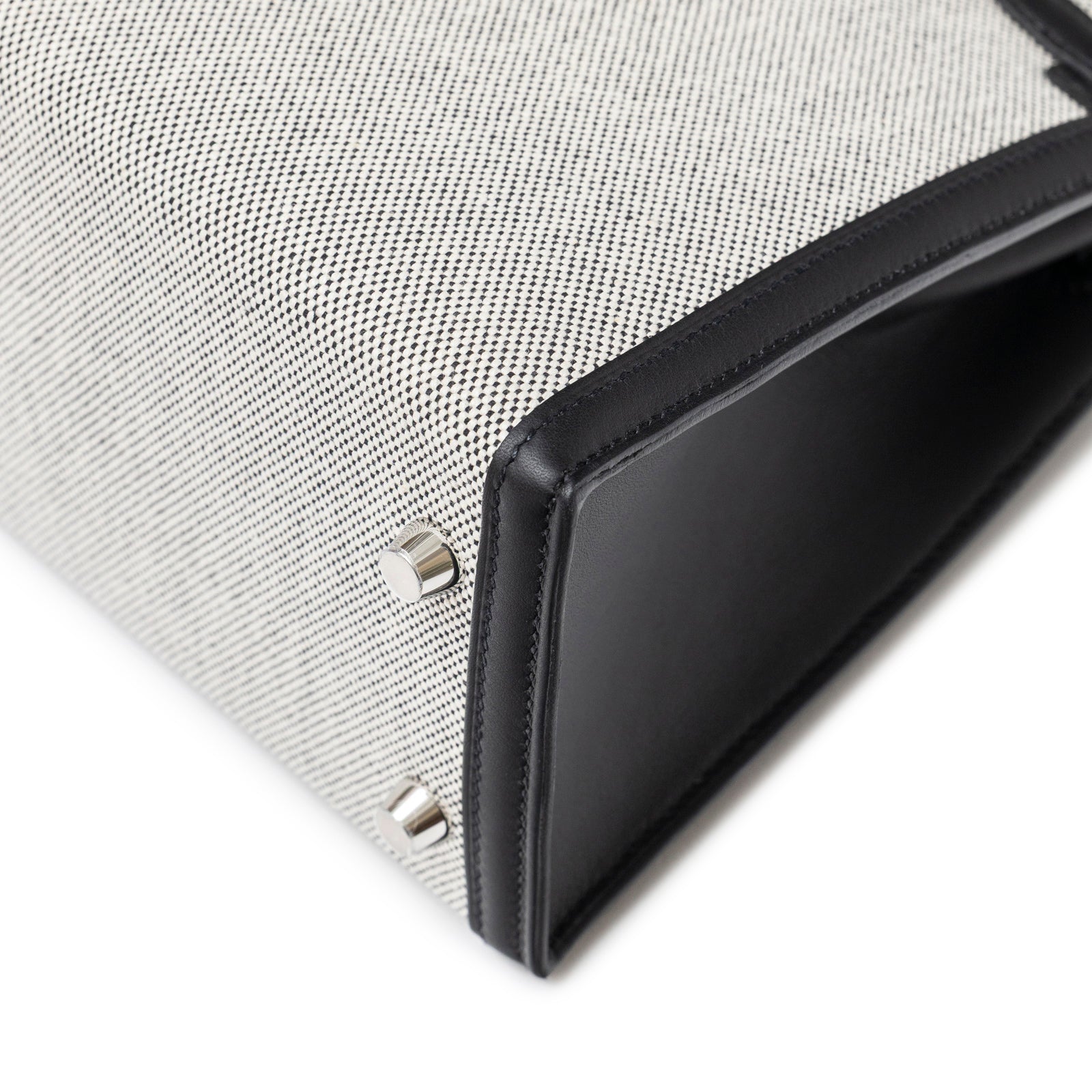Close-up angled shot of bottom corner with black leather trim and palladium hardware on Hermès Kelly 25 Sellier Ecru Black Swift Toile H Canvas Swift Palladium Hardware