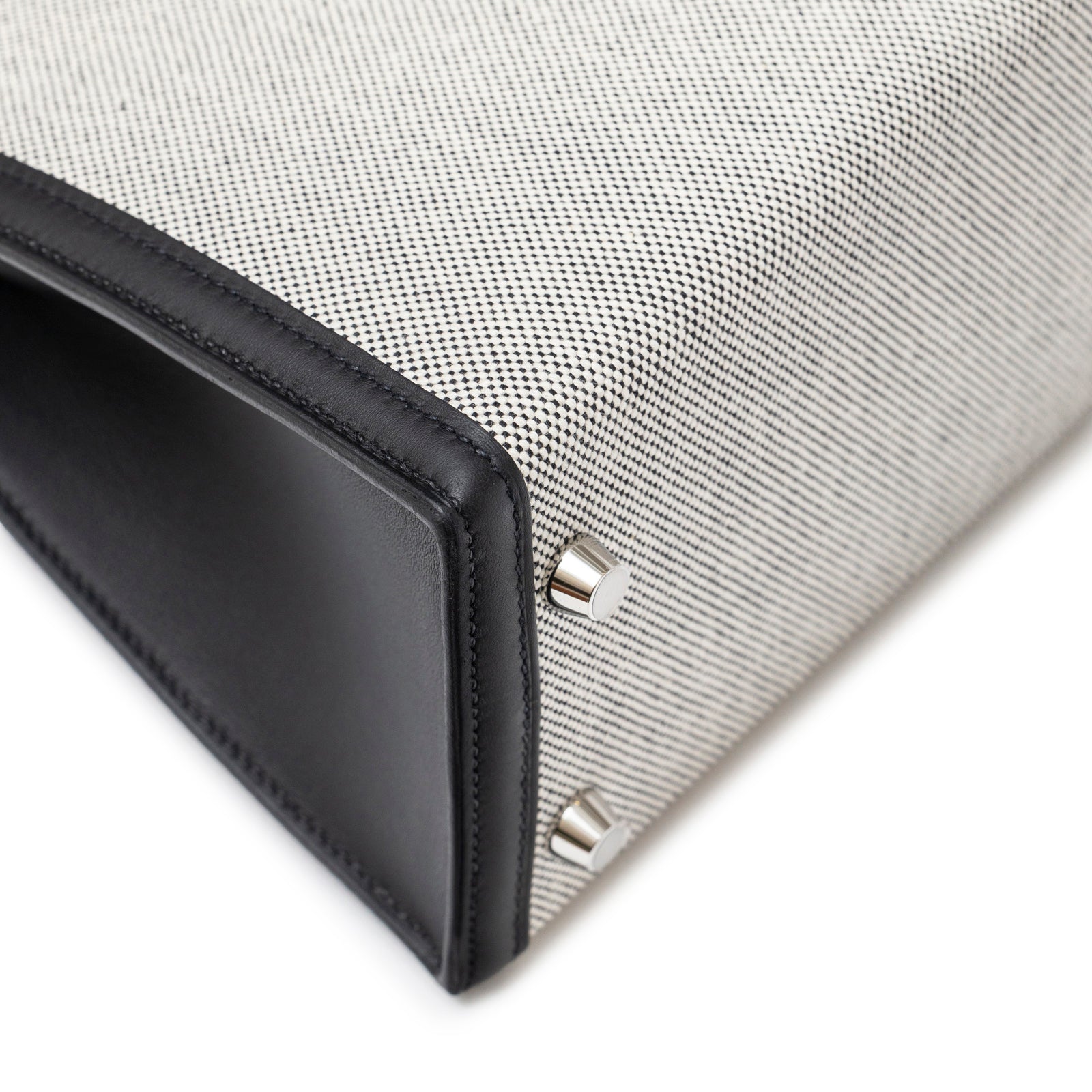 Close-up angle of base and corner with palladium feet on Hermès Kelly 25 Sellier Ecru Black Swift Toile H Canvas Swift Palladium Hardware
