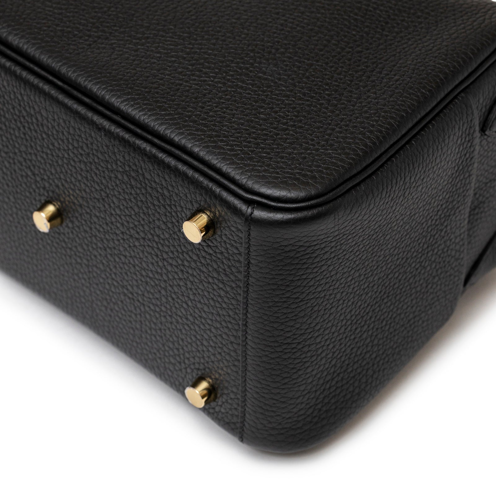 Close-up of Hermès Lindy 26 Black Clemence Gold Hardware showing textured leather and gold protective feet on bottom corner.