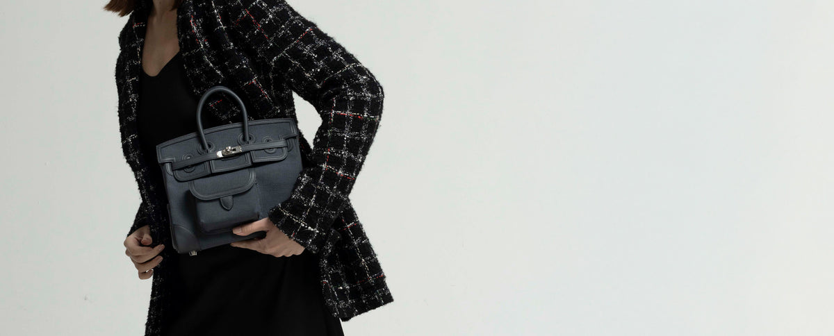 Gray structured handbag with top handles held by a woman in a black tweed jacket