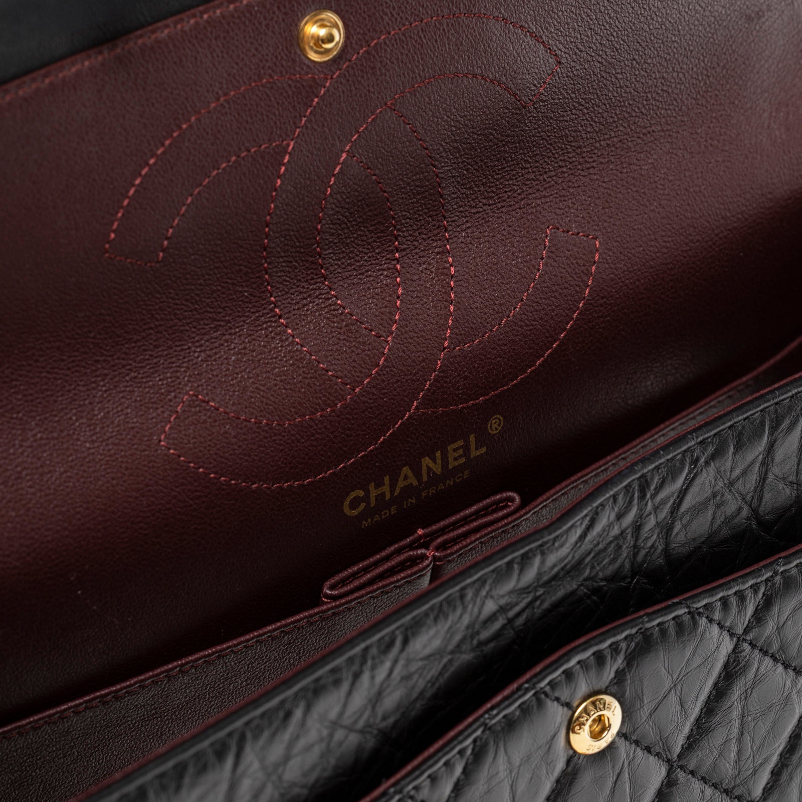Close-up of the interior burgundy leather with logo and snap closure on Chanel 2.55 Reissue 226 Flap Black Aged Calfskin Brushed Gold Hardware