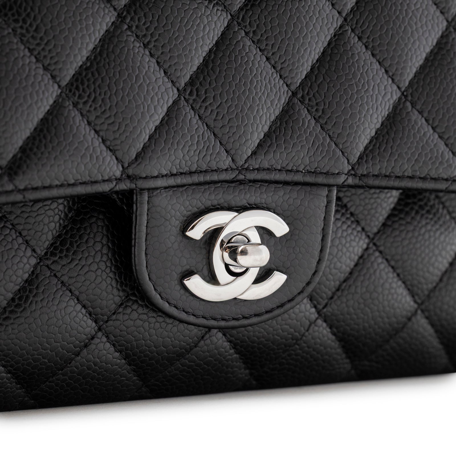 Close-up of silver CC turn-lock clasp on quilted black caviar leather of Chanel Medium Classic Flap Bag Black Caviar Palladium Hardware