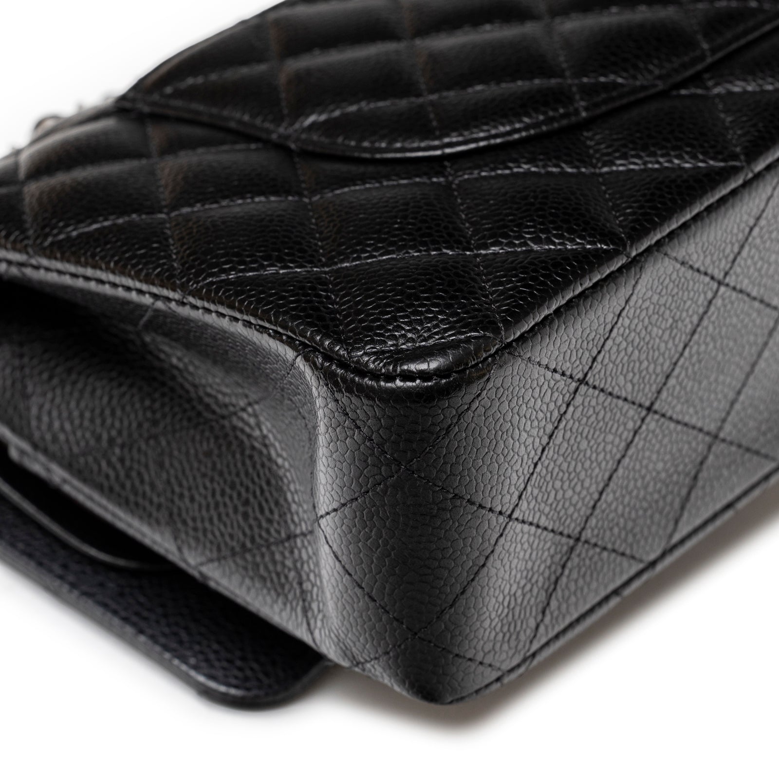 Close-up angled view of bottom corner showing grainy leather texture and diamond quilt pattern on Chanel Medium Classic Flap Bag Black Caviar Palladium Hardware