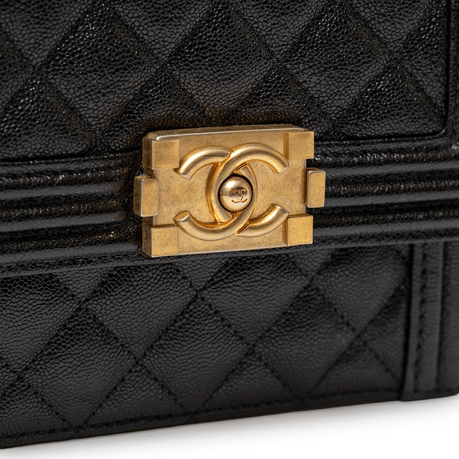 Close-up of brushed gold hardware clasp on Chanel North South Boy Flap Bag Black Caviar leather textured surface