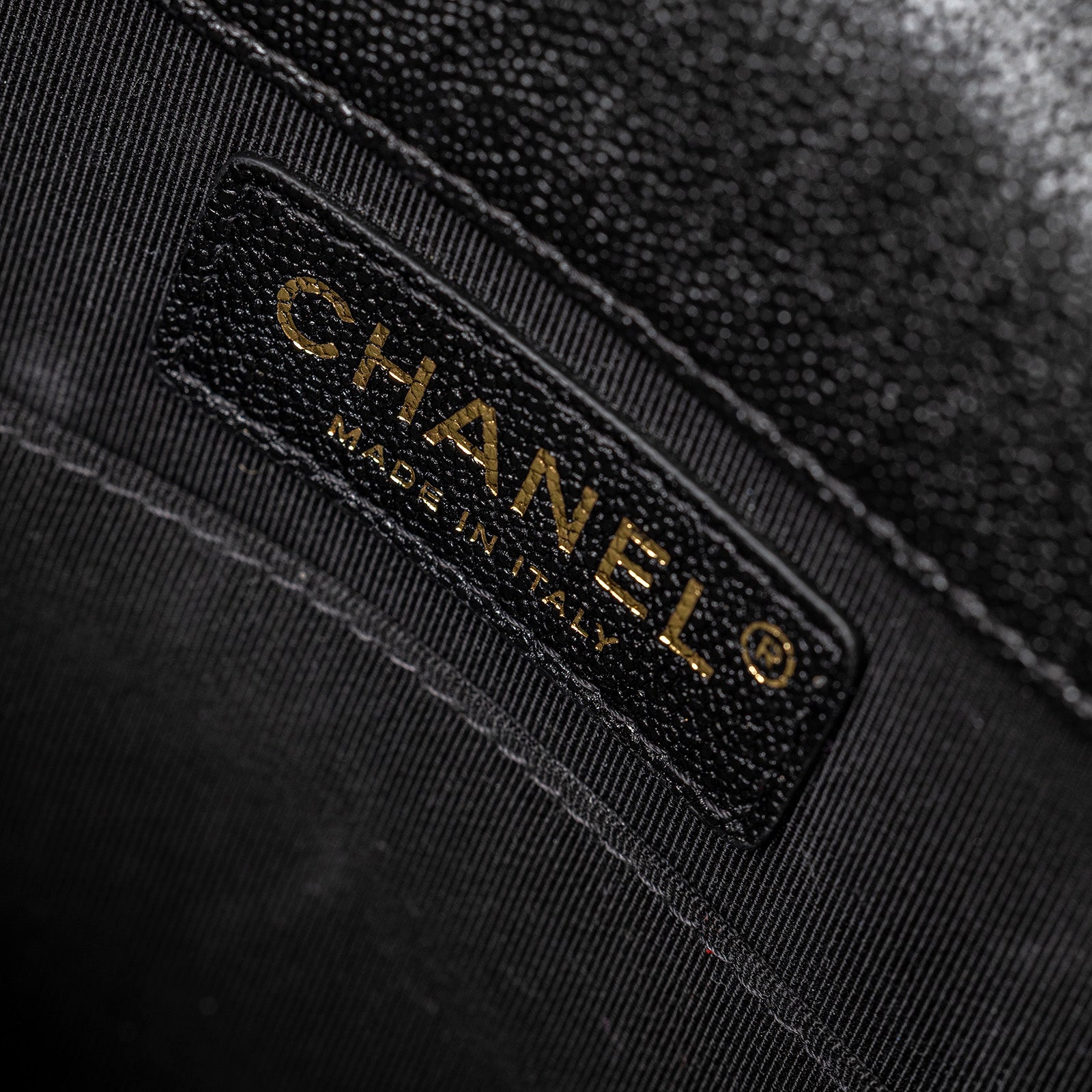Close-up interior shot of Chanel North South Boy Flap Bag Black Caviar Brushed Gold Hardware showing the leather brand label and stitching detail.