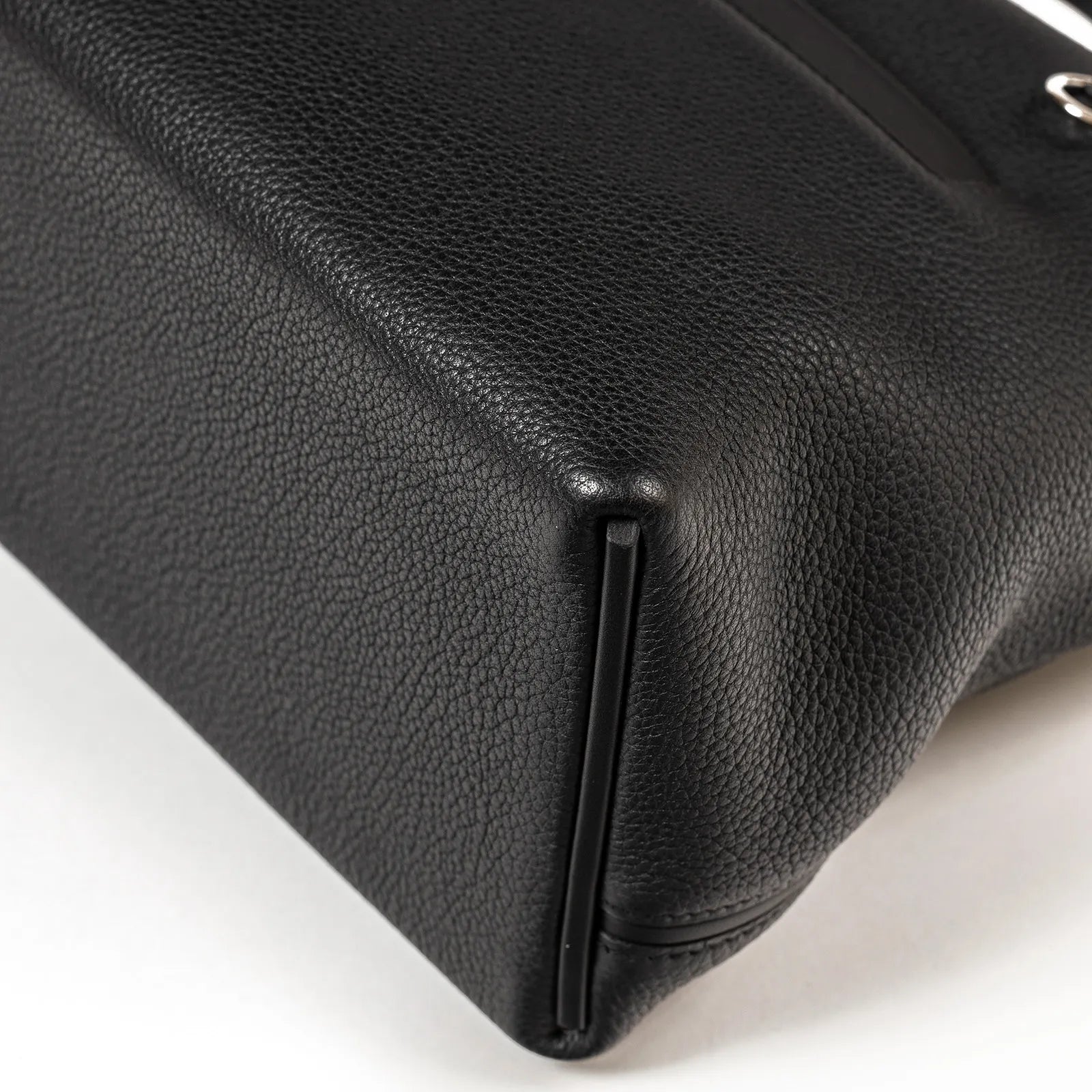 Close-up angled view of black Taurillon leather corner with visible stitching and structure of the bag base