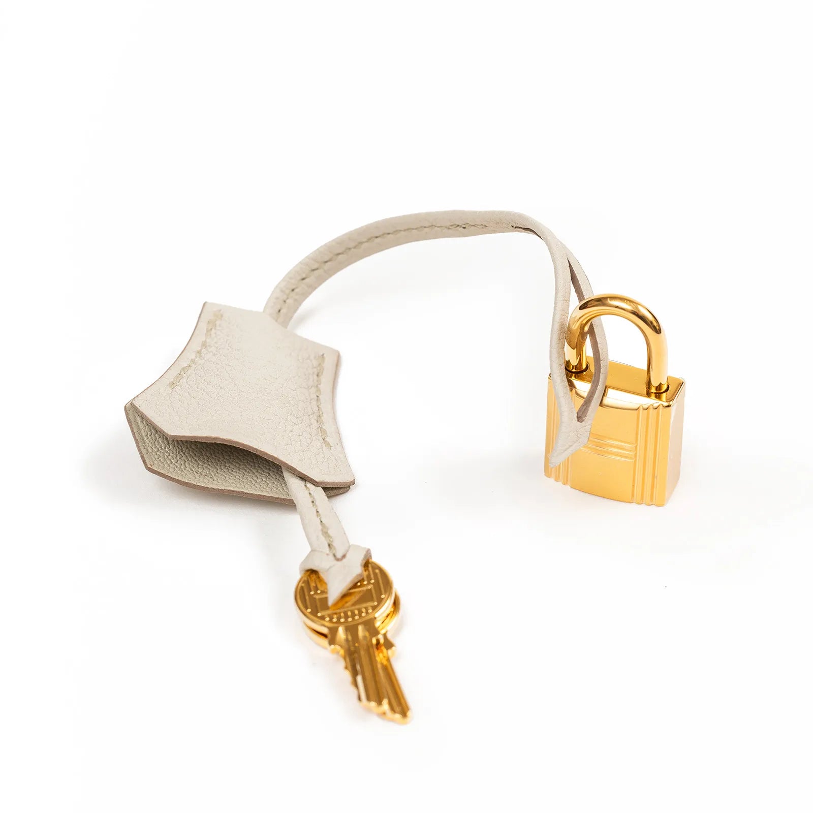 Close-up of gold lock and key attached to beige leather clochette for Birkin 25 Beton Togo handbag