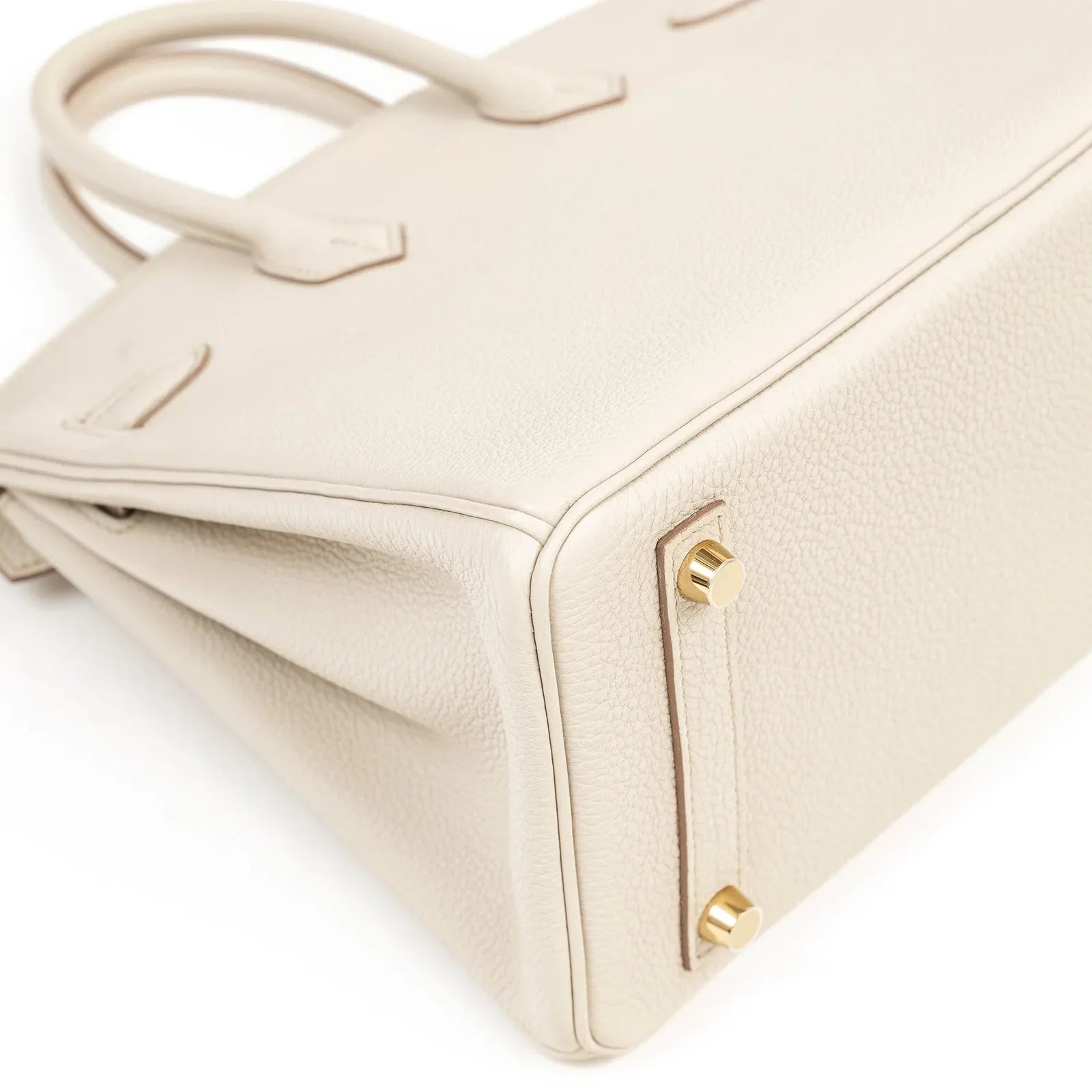 Close-up angled view of beige textured leather Birkin 25 bottom corner with gold hardware studs visible