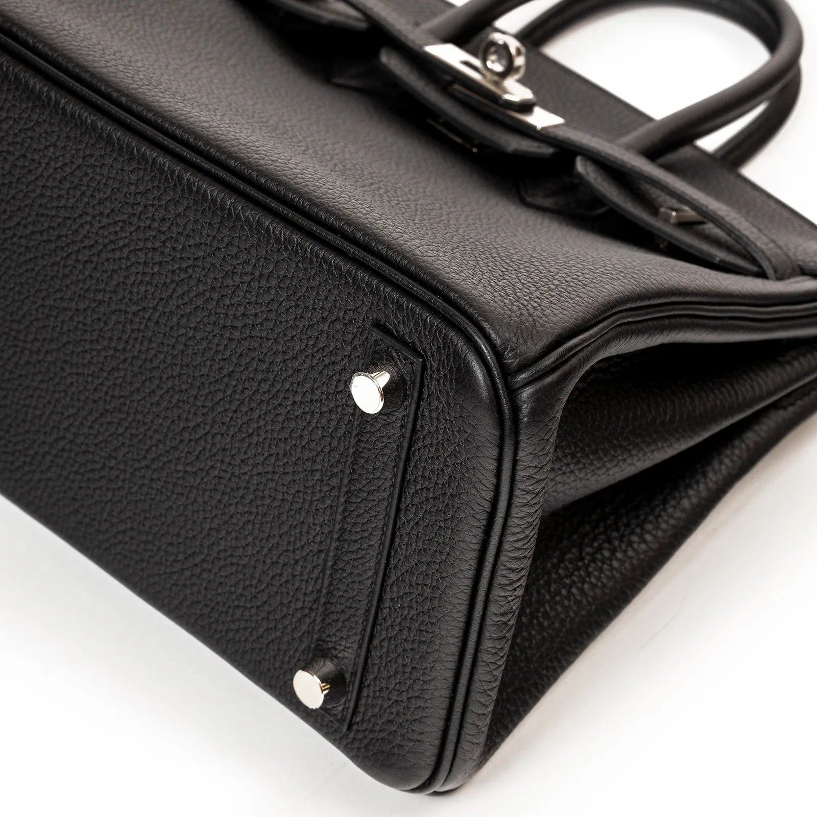 Close-up angled shot of black Togo leather Hermès Birkin 25 base with palladium hardware feet and stitching detail