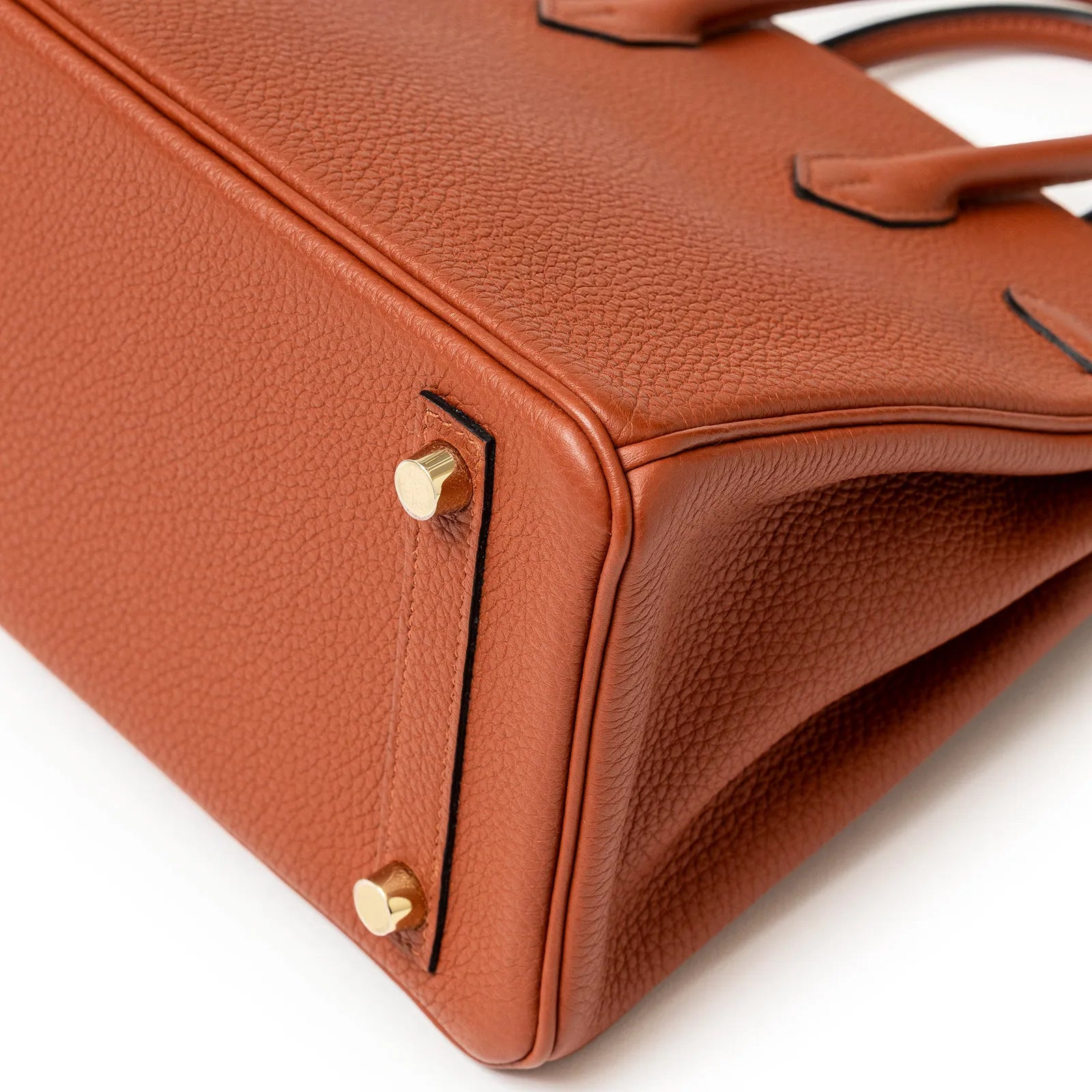 Close-up shot of the bottom corner of a copper leather bag with gold metal feet and textured leather grain.