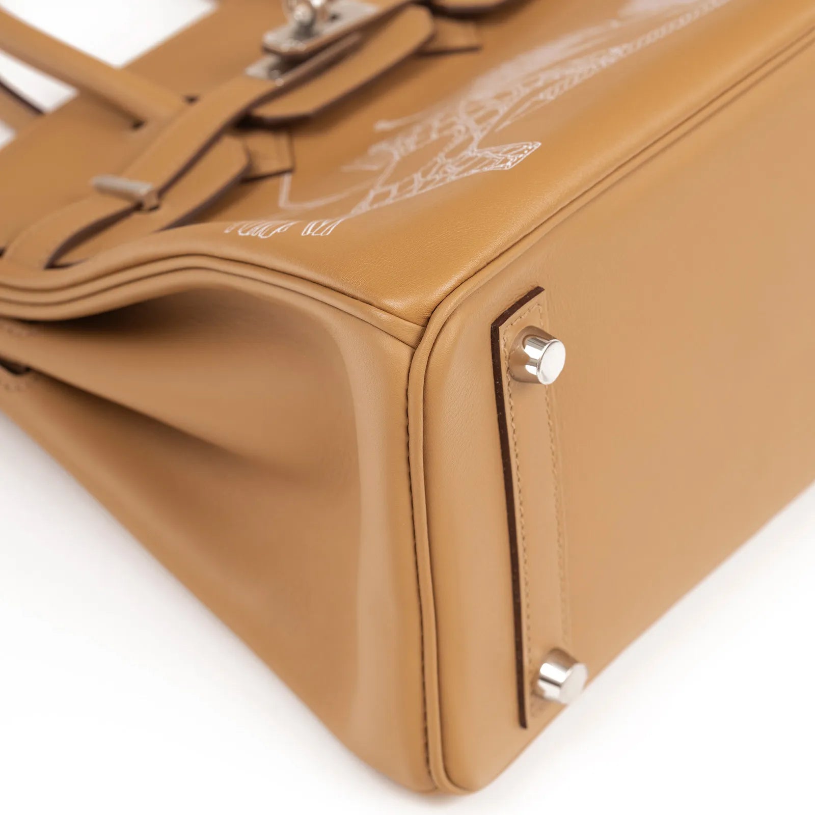 Close-up angled shot of Hermès Birkin 25 in biscuit leather showing detailed palladium hardware on the base