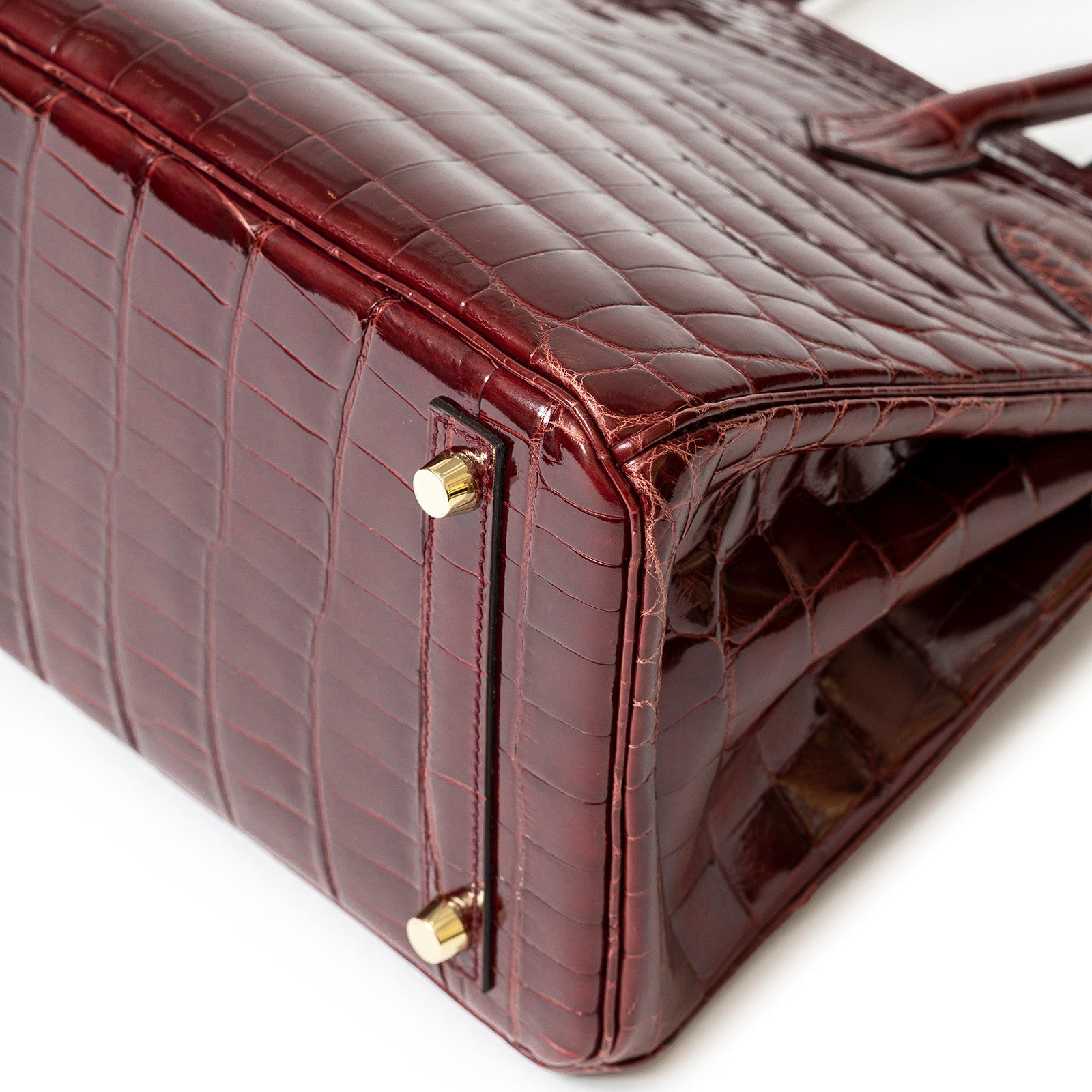 Close-up angled view of Hermès Birkin 30 in shiny Bourgogne Niloticus crocodile with gold hardware feet details