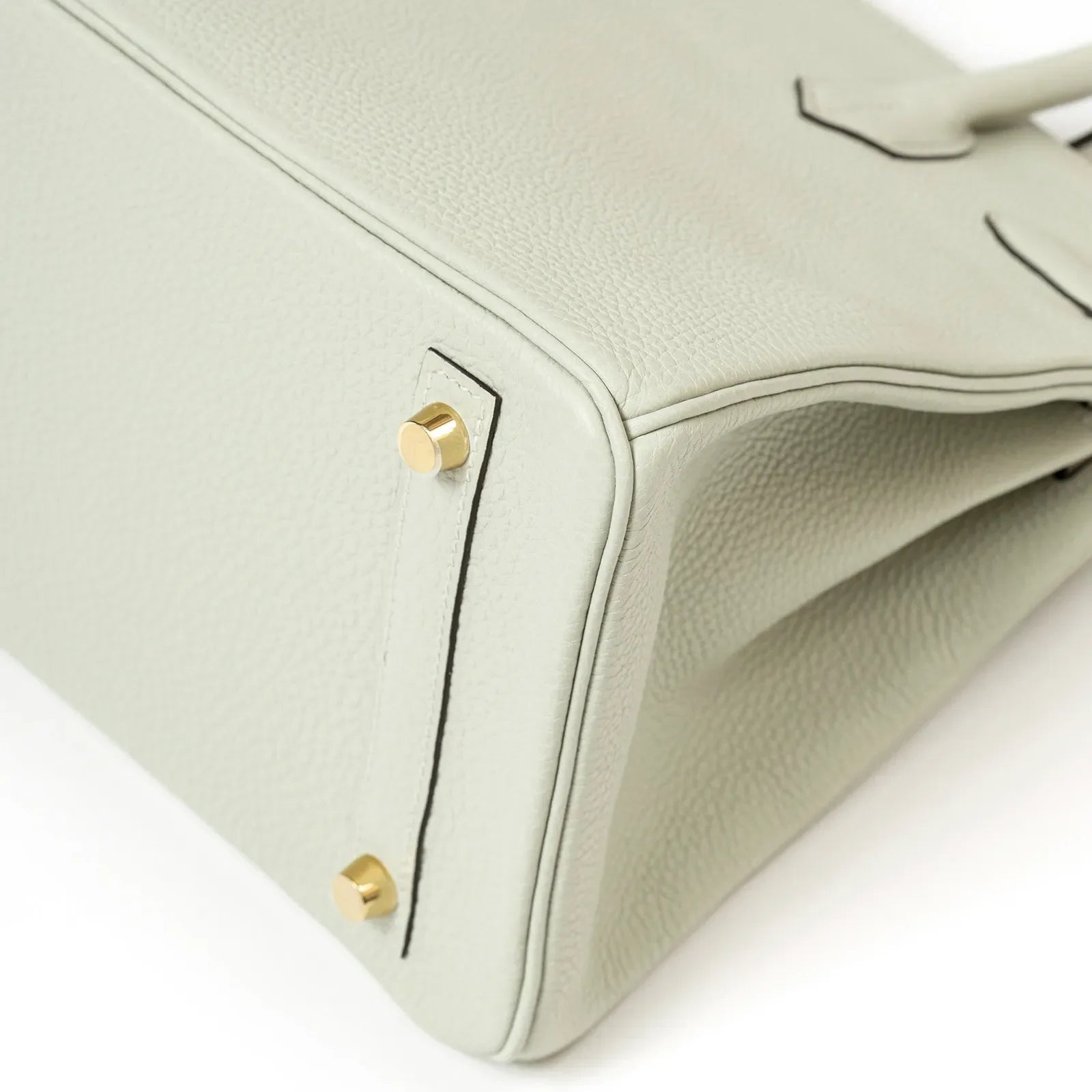 Close-up of the bottom corner showing Gris Neve Togo leather texture and gold hardware feet on Birkin 30 bag
