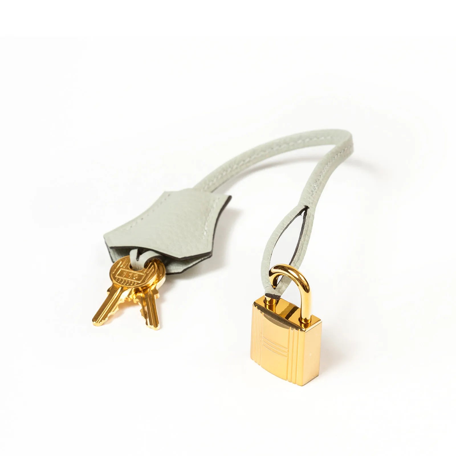 Close-up of Hermès Birkin 30 gold padlock and matching keys in light gray leather clochette accessory