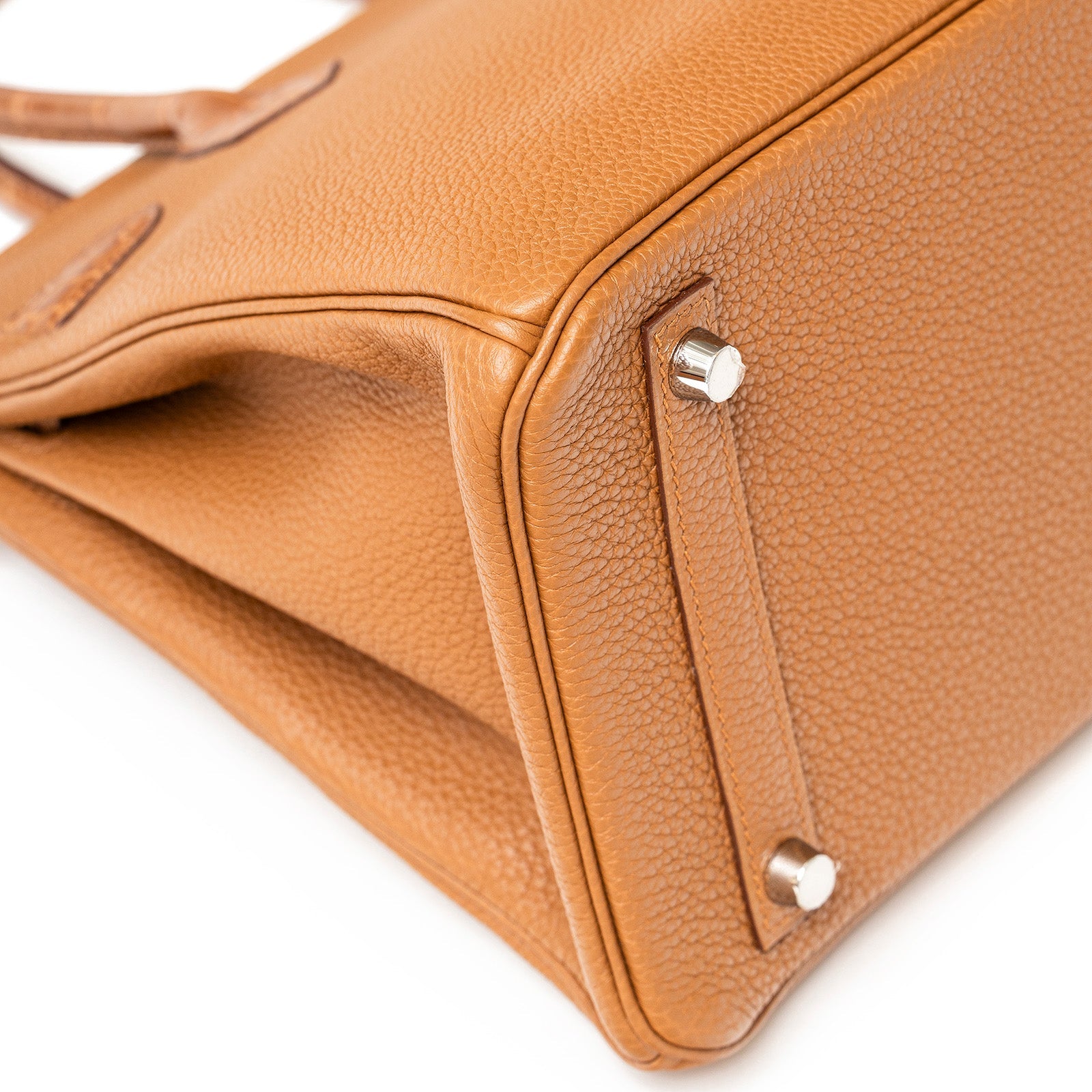 Close-up angled view of the Hermès Birkin 30 base in gold togo leather showing palladium feet and stitching details.