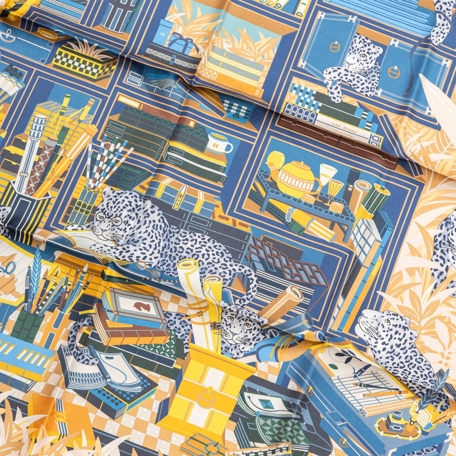 Close-up angled view of Hermès Carre 90 Double Face Les Douze Leopards Blue Beige Jaune silk scarf showing detailed leopard and bookshelf pattern