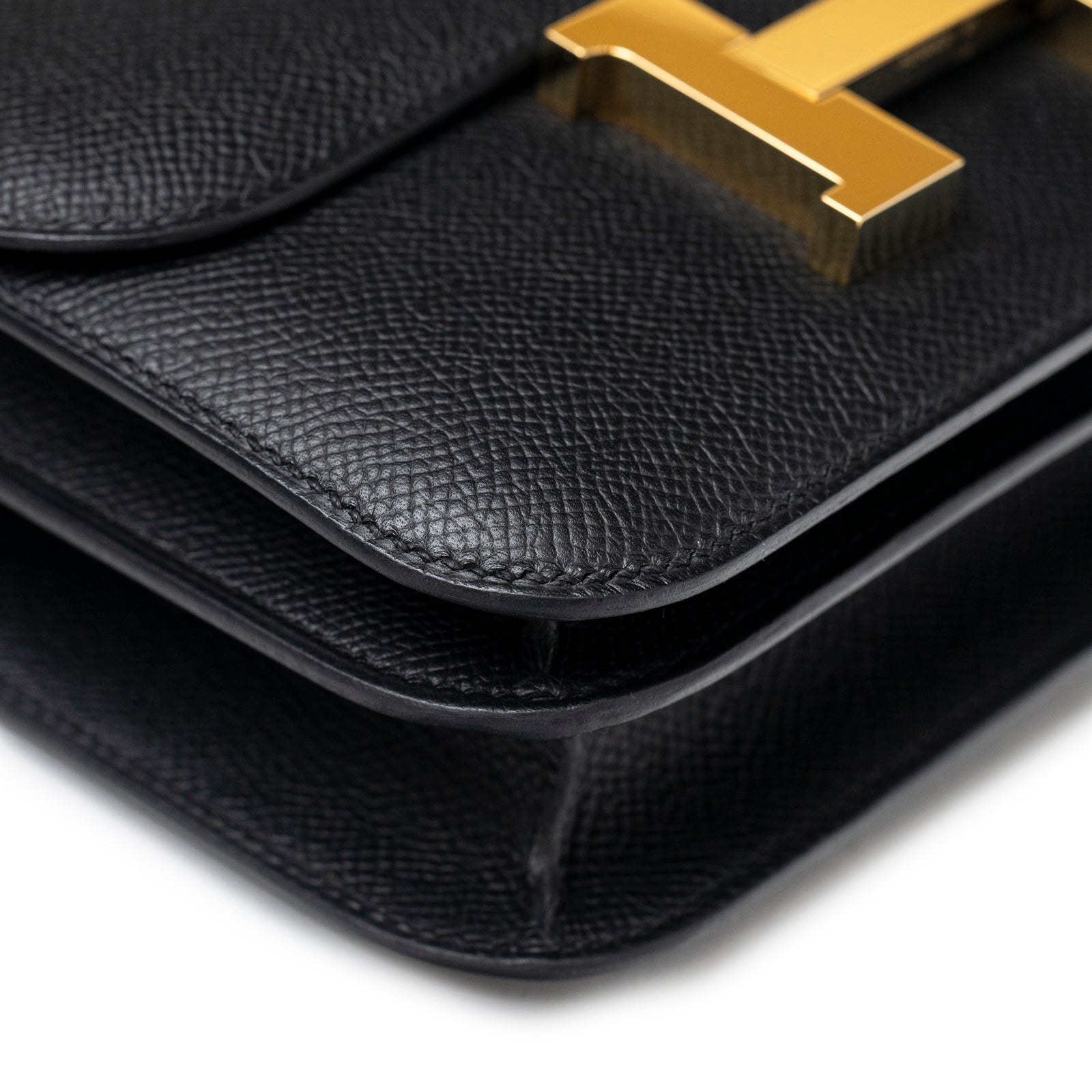 Close-up angled view of Hermès Constance 18 Black Epsom Gold Hardware showing textured leather and gold clasp detail.