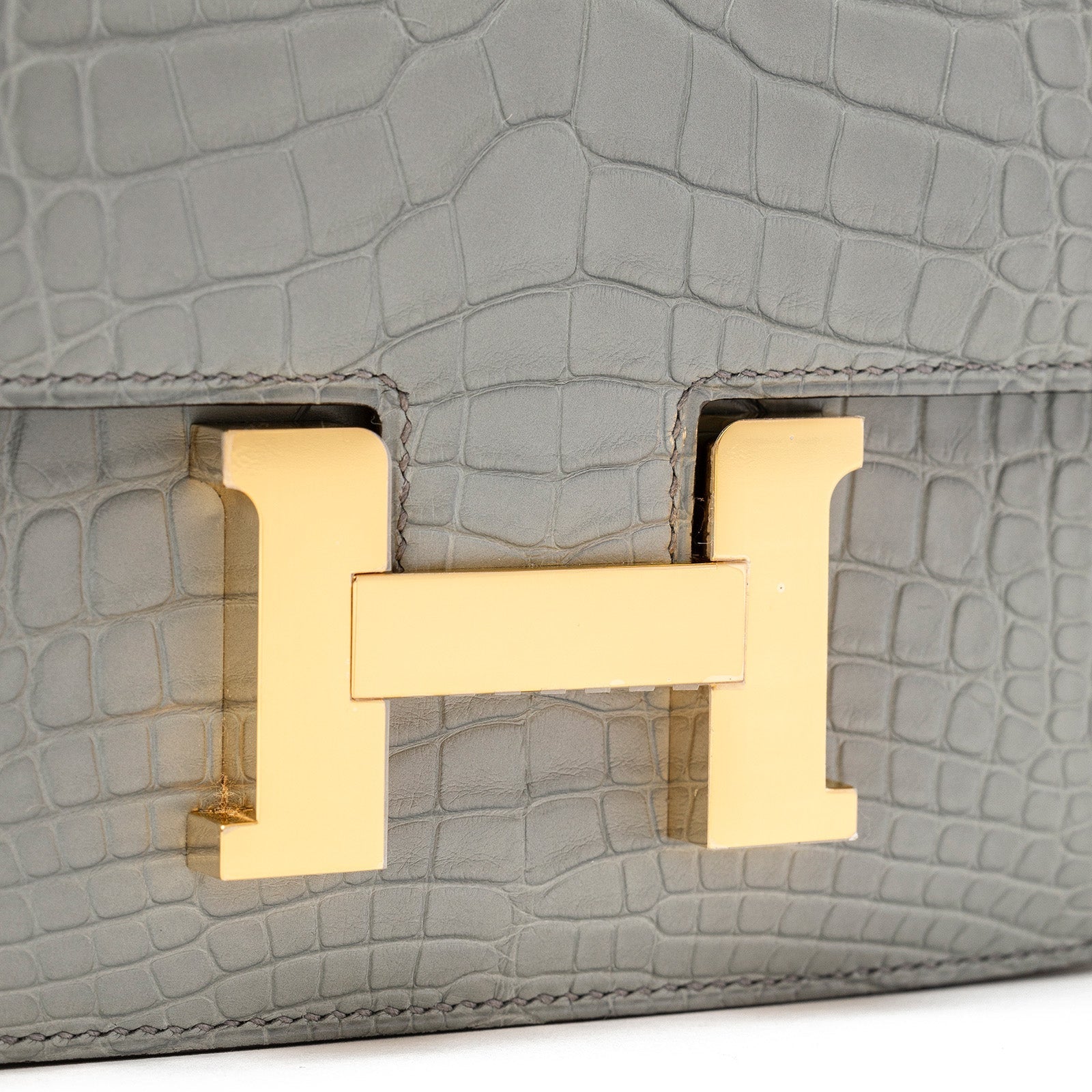 Close-up of gold hardware clasp on Hermès Mini Constance 18 Gris Ciment Matte Alligator bag