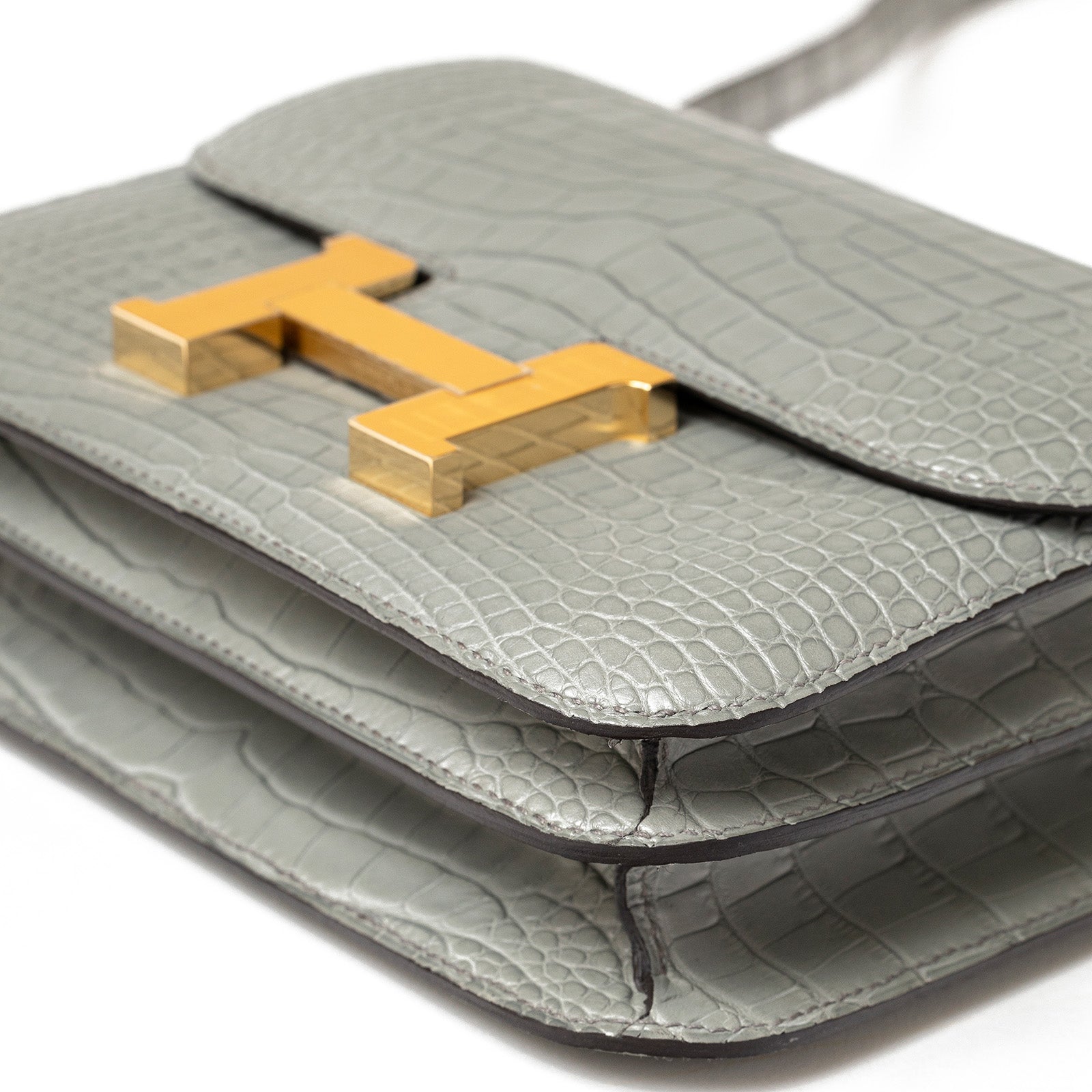 Close-up angled shot of Hermès Mini Constance 18 Gris Ciment Matte Alligator Gold Hardware showing texture and clasp details