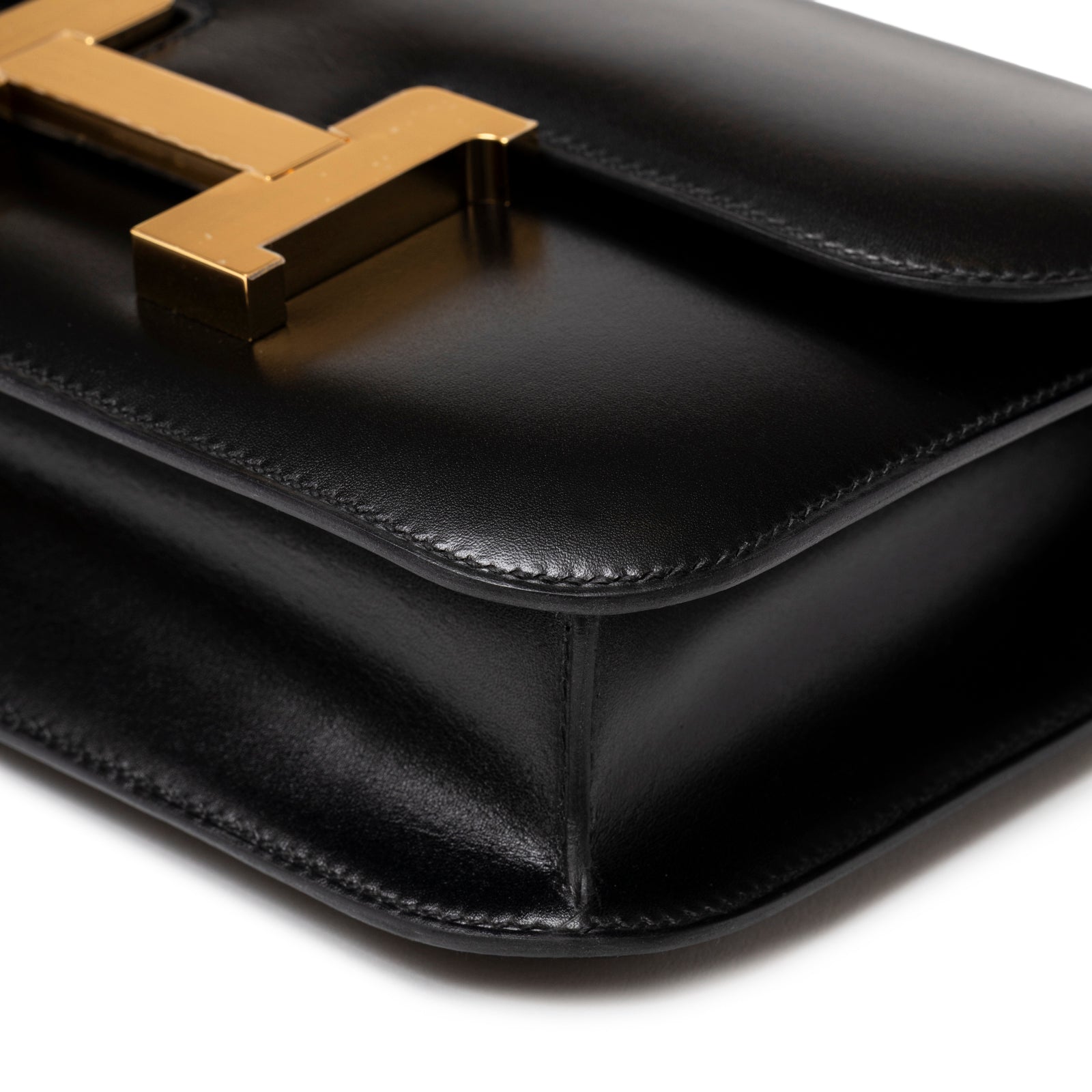 Close-up angled view of Hermès Constance 24 Black Box Gold Hardware highlighting sleek leather and polished gold clasp detail
