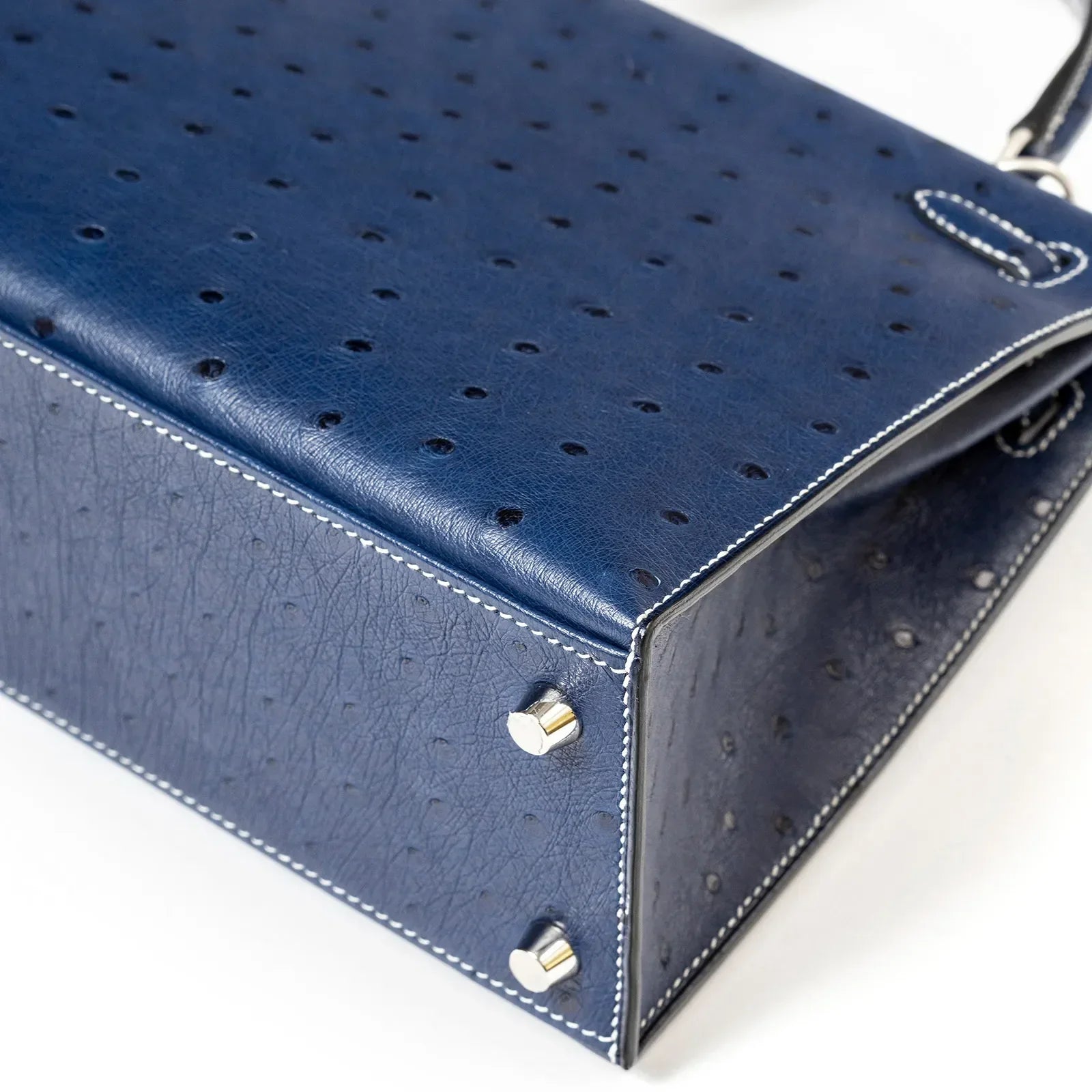 Close-up angled shot of Hermès Horseshoe Kelly 25 Sellier Ostrich Blue Iris/Gris Brushed Palladium Hardware base and stitching detail