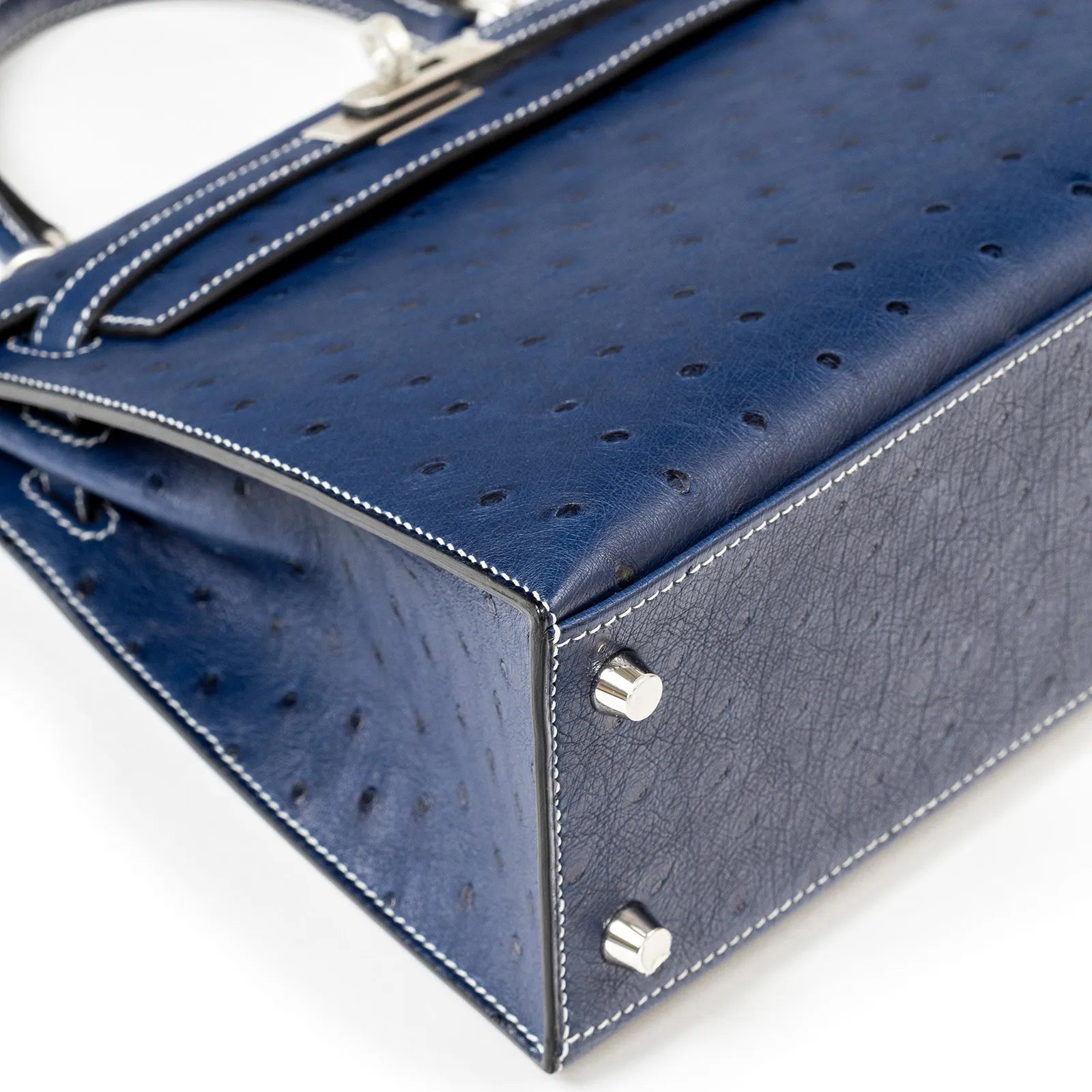 Close-up of the base corner showing detail on Hermès Horseshoe Kelly 25 Sellier Ostrich Blue Iris/Gris Brushed Palladium Hardware