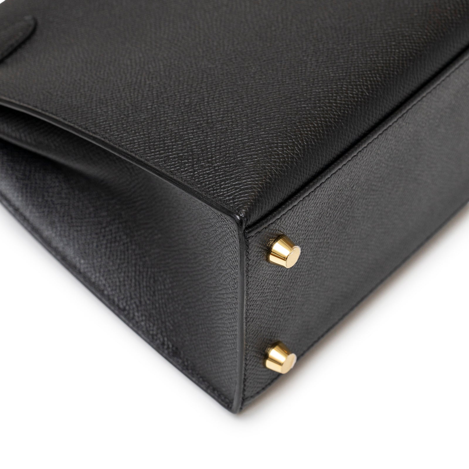 Close-up of the corner details and gold hardware feet on the Hermès Kelly 25 Sellier Black Epsom Gold hardware handbag.