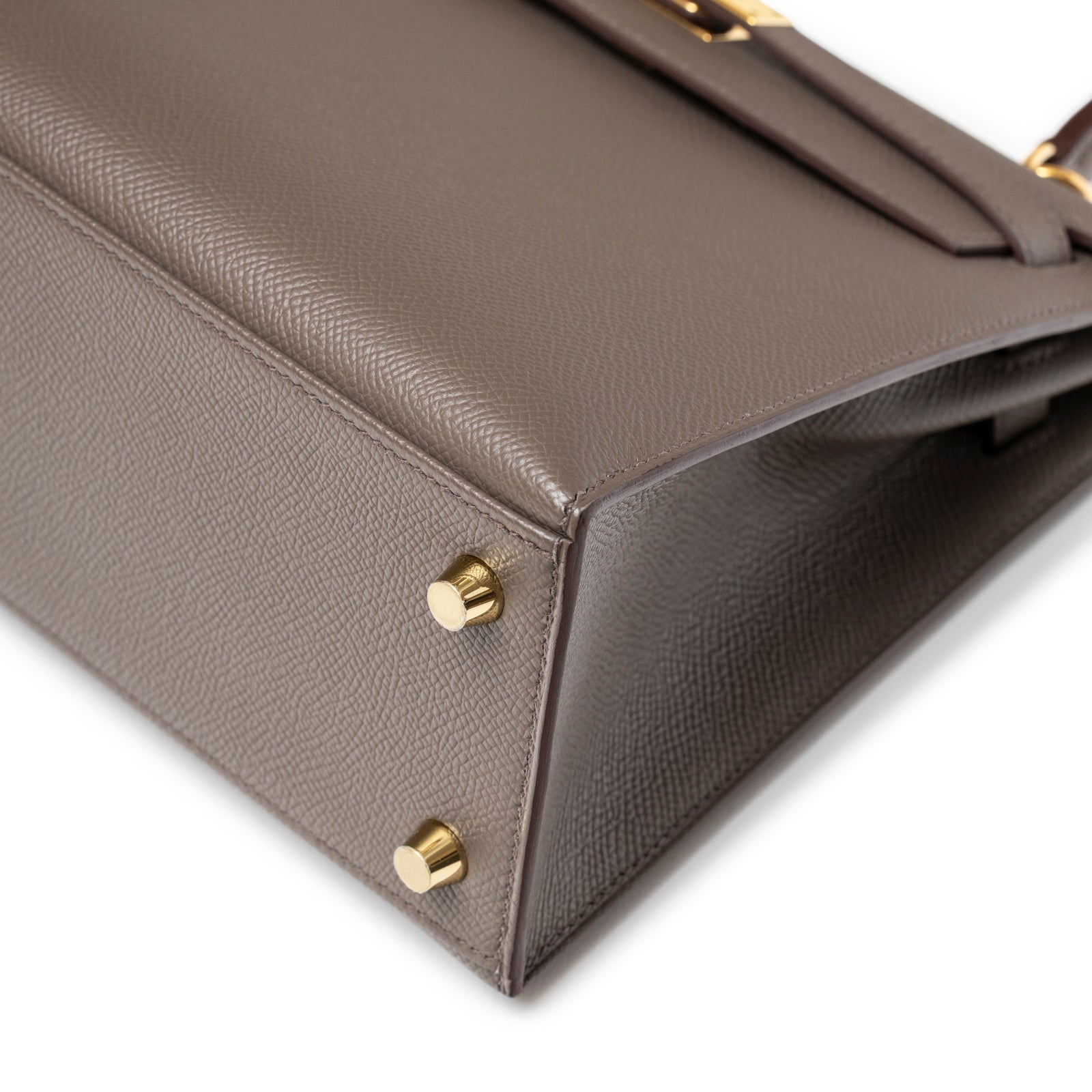 Close-up of the base corner on Hermès Kelly 25 Sellier Etain Epsom Gold Hardware showing leather texture and gold protective feet detail