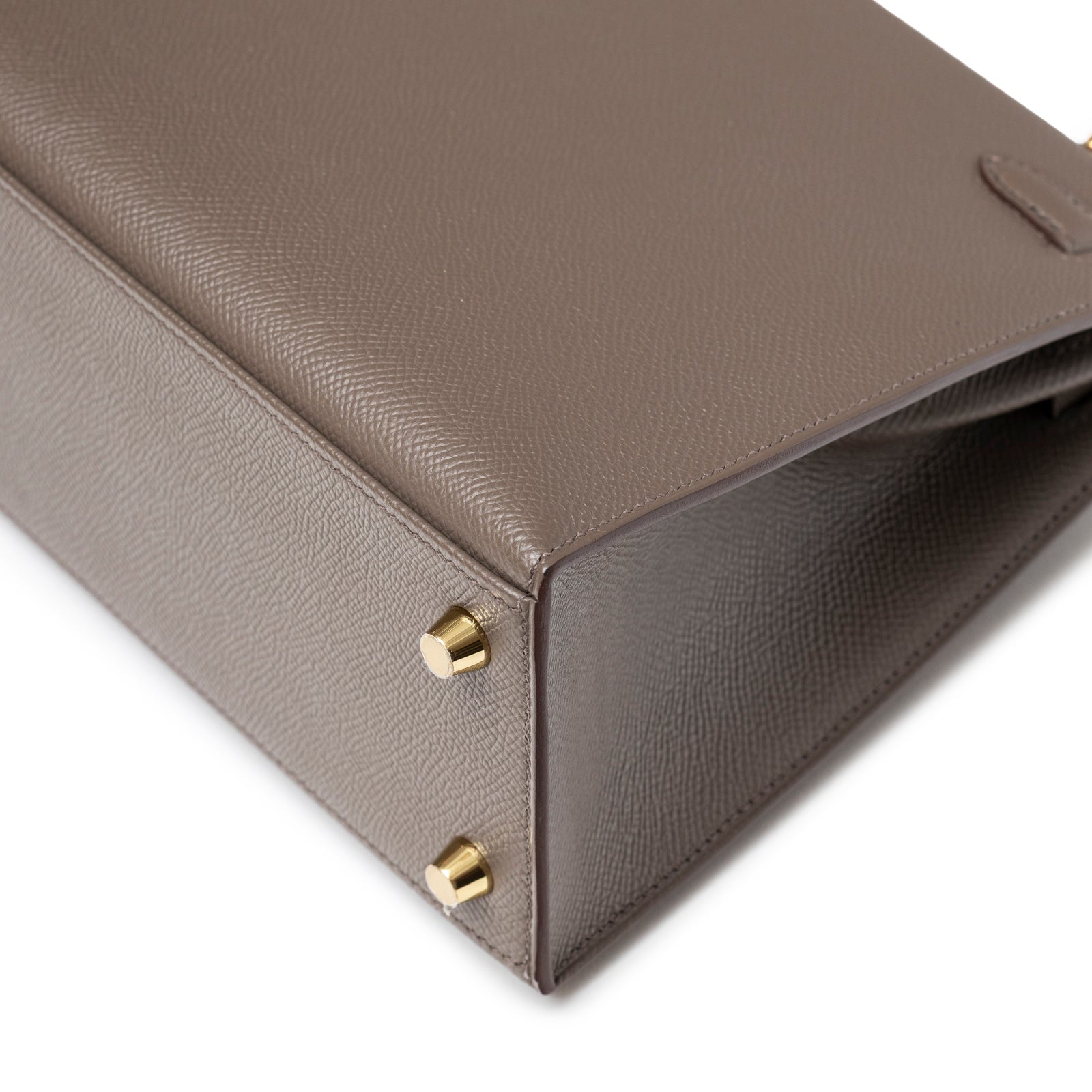 Close-up of base corner on Hermès Kelly 25 Sellier Etain Epsom Gold Hardware showing textured leather and gold feet detail