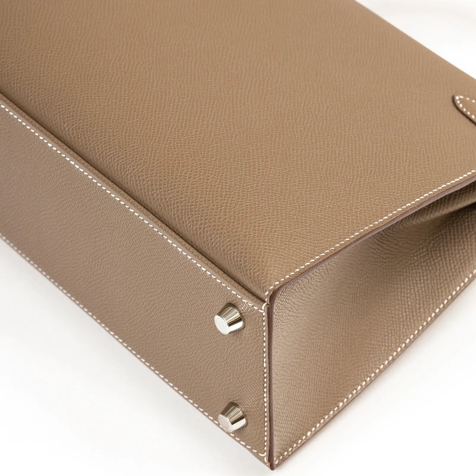 Hermès Kelly 25 Sellier Etoupe Epsom Palladium Hardware handbag base with metallic studs on a white background.