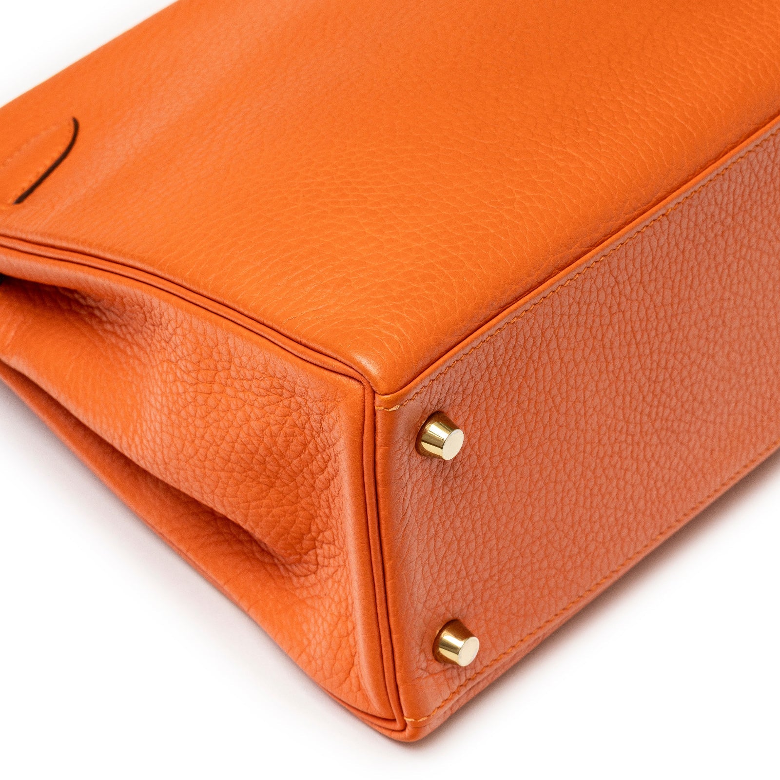 Close-up of bottom corner showing textured Clemence leather and gold hardware of Hermès Kelly 28 Retourne Orange Clemence Gold Hardware