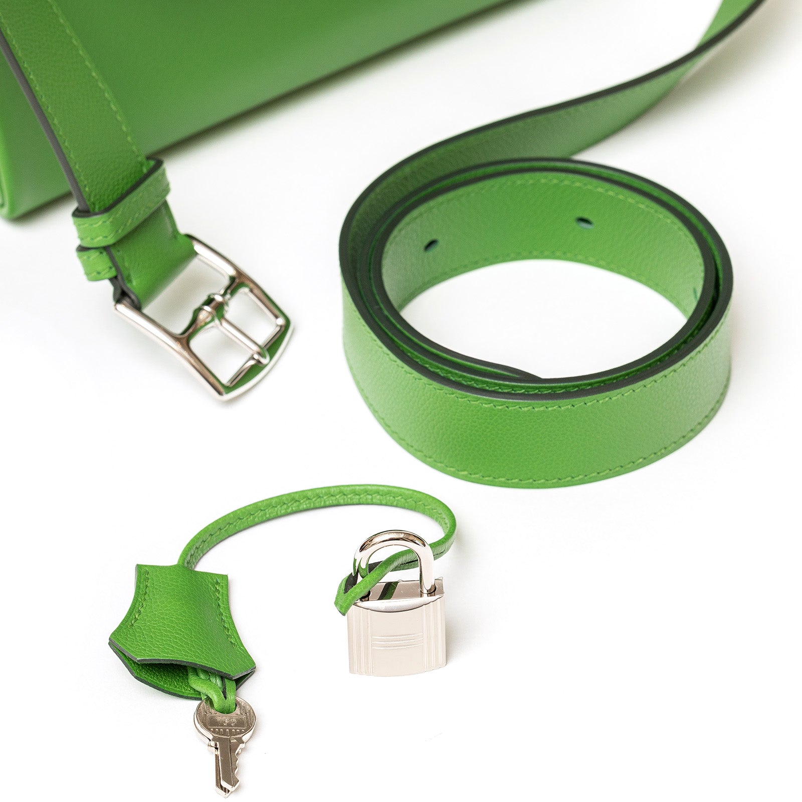 Green bag strap and hardware set with silver buckle and lock detail, top-down view.